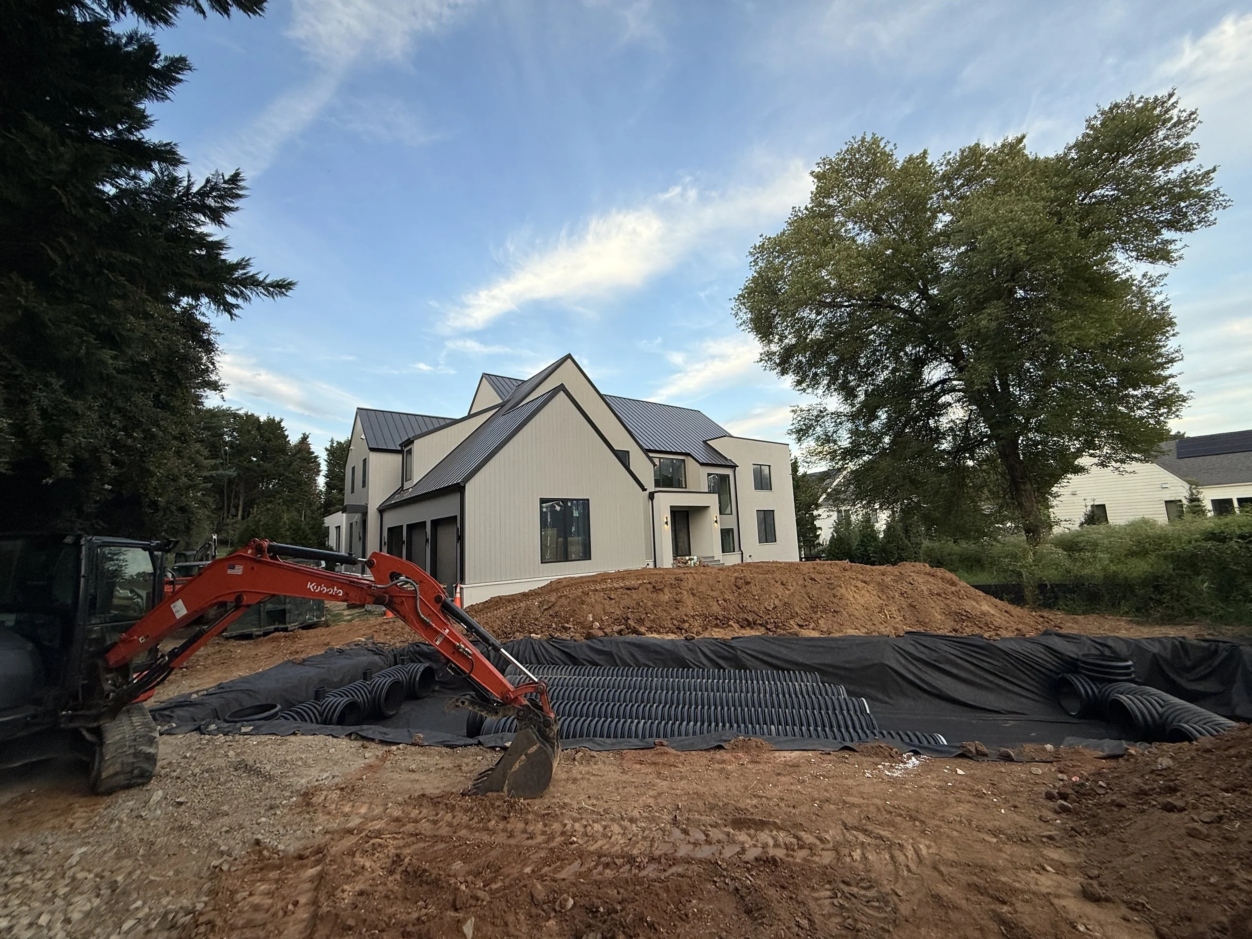 Residential underground stormwater detention field wrapped in geotextile with a Kubota excavator beside a modern Northern Virginia farmhouse.