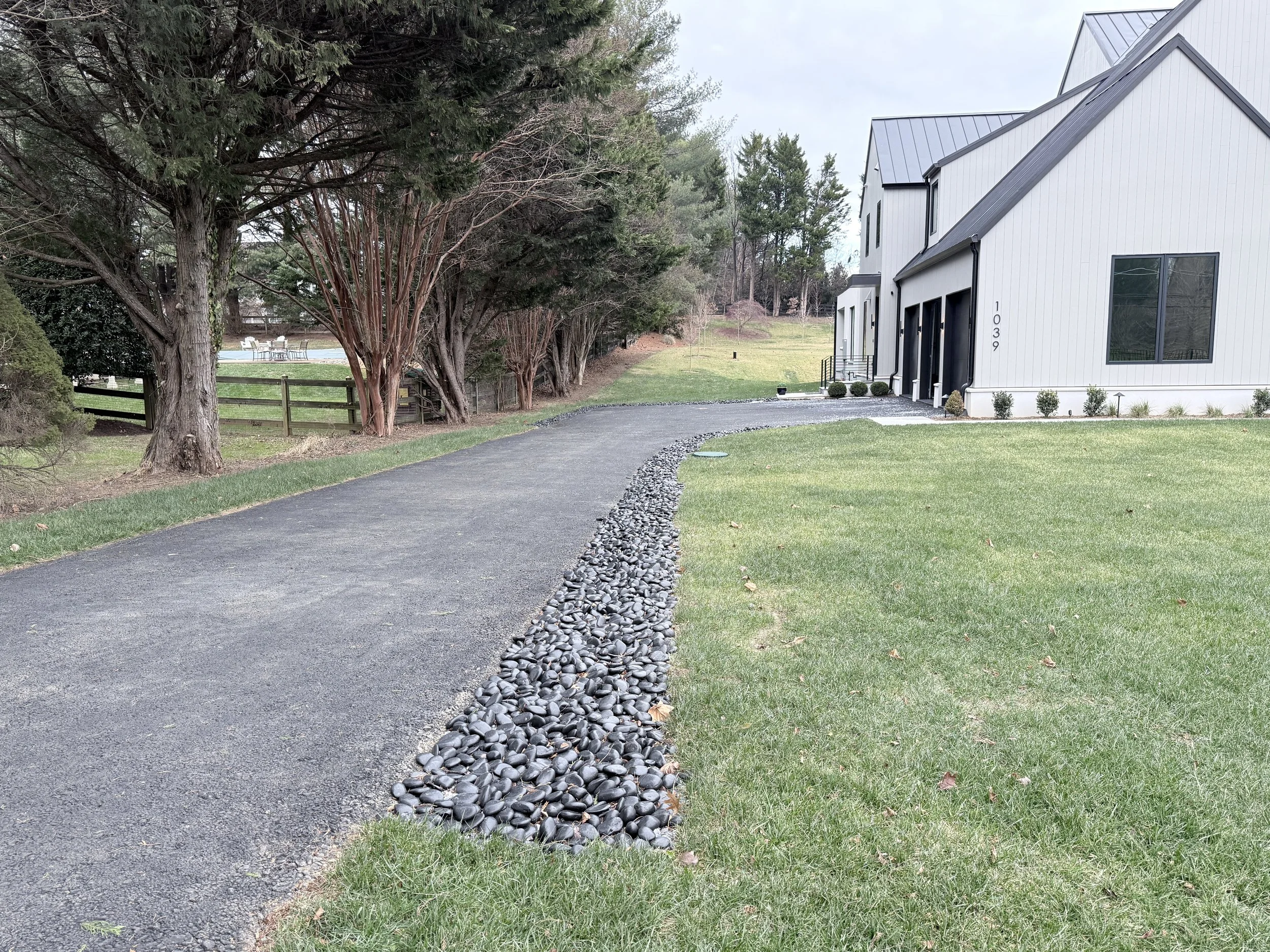 Finished driveway with a black river-rock drainage swale channeling stormwater runoff at a Northern Virginia home by Capital Stormwater Services.