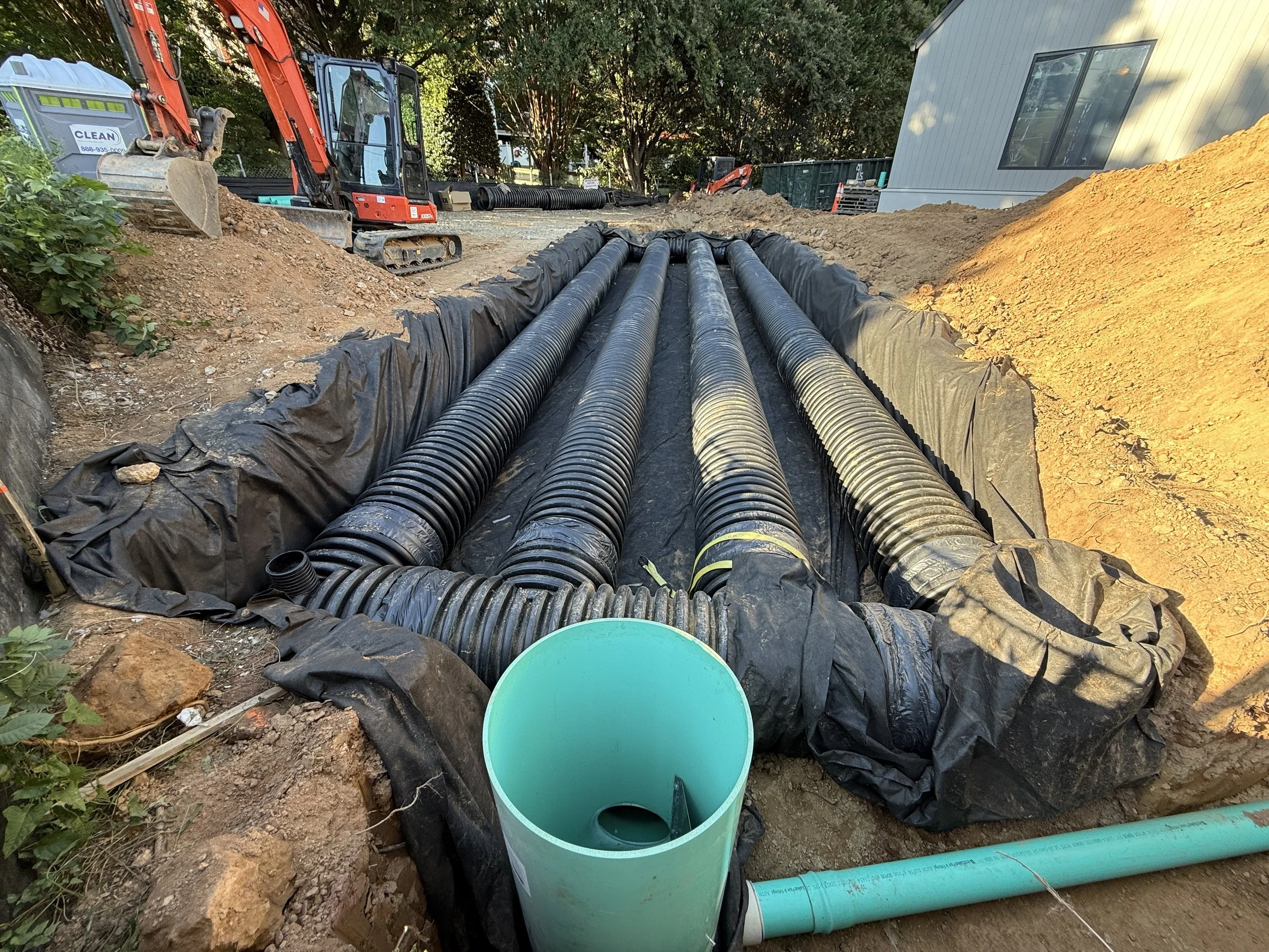 HDPE underground detention pipes wrapped in geotextile with a riser and green PVC outlet during a residential stormwater installation in Northern Virginia.