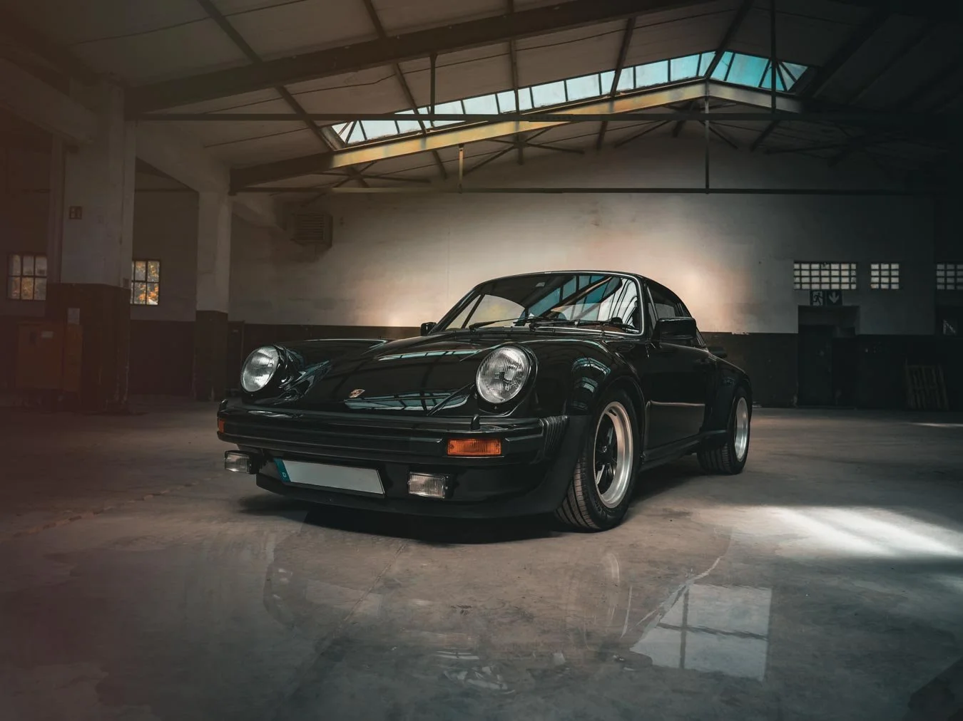 Ein schwarner Porsche 911 in einer Lagerhalle mit hohem Dach und großen Fenstern.