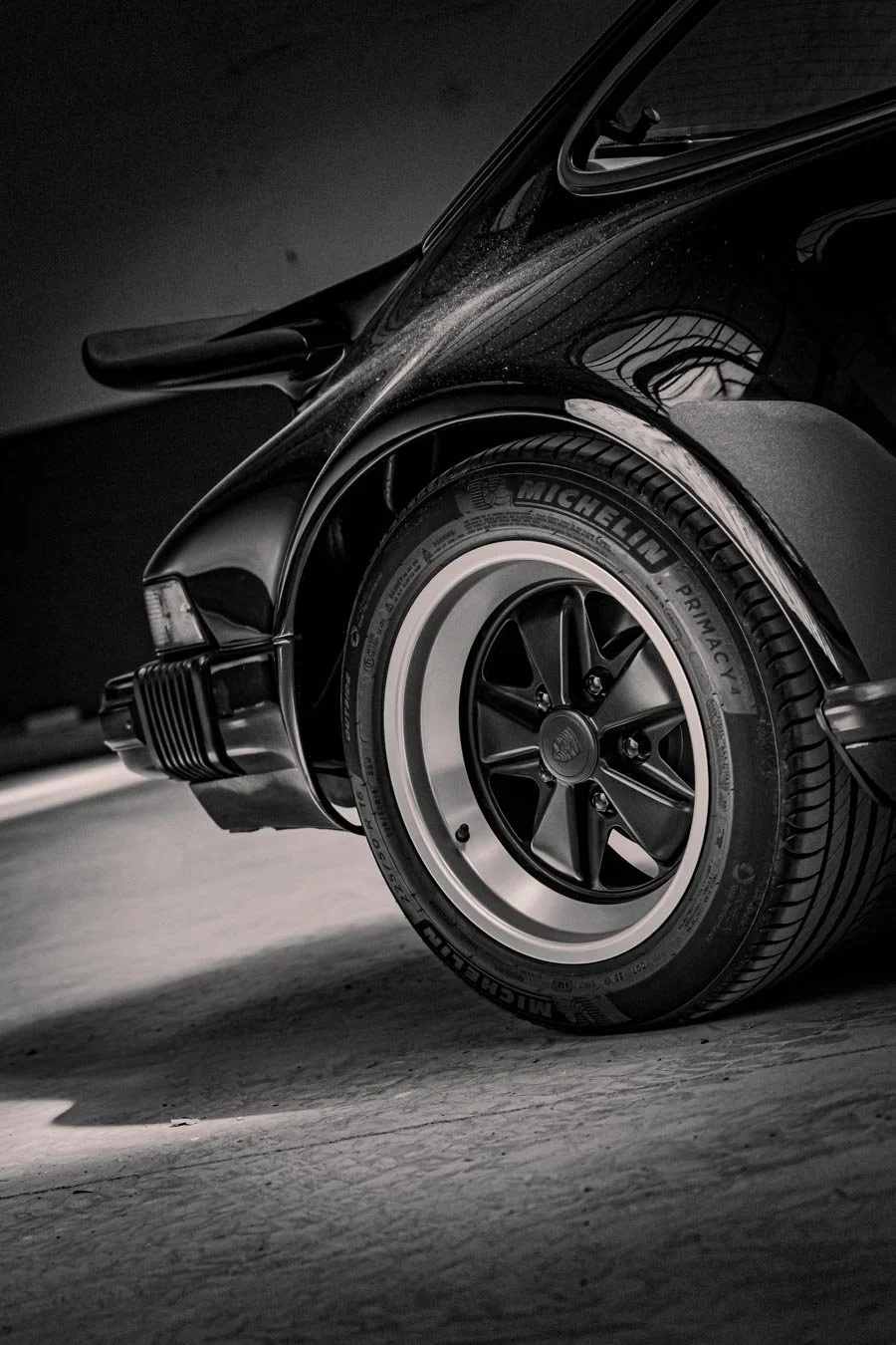 Nahaufnahme eines schwarzen Sportwagens, Fokus auf das vordere Rad mit Michelin-Reifen, in Schwarz-Weiß-Optik.