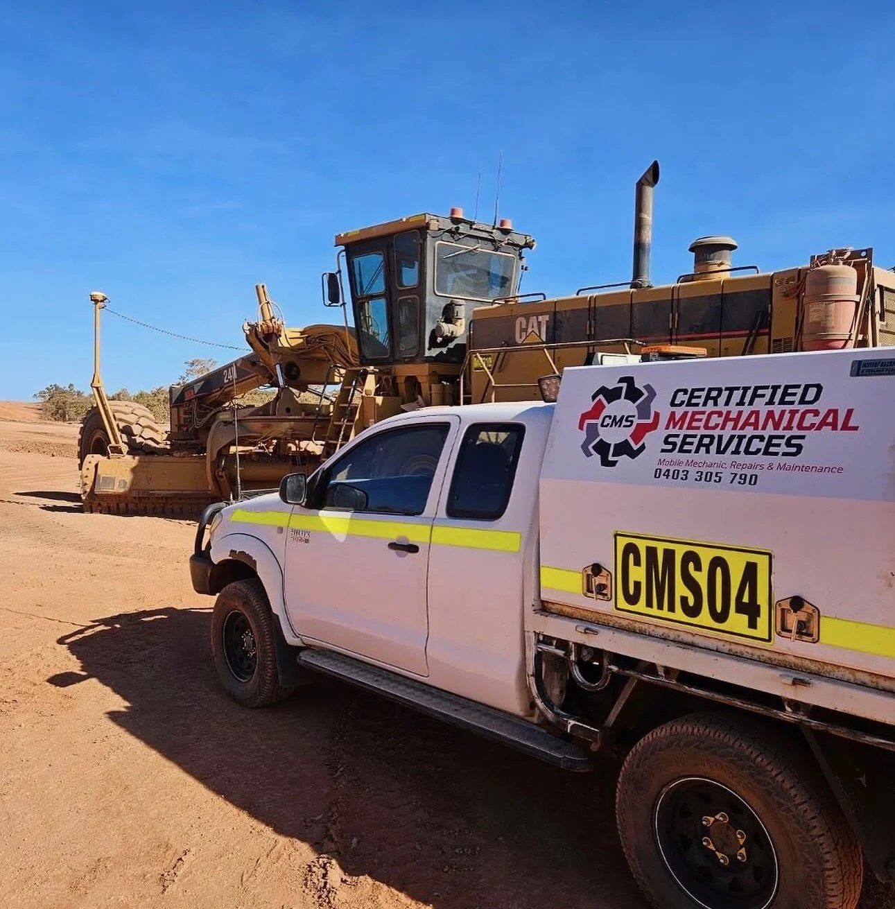 A large yellow bulldozer on a dirt construction site with a white service vehicle in front of it. The service vehicle has signage for "Certified Mechanical Services" and a yellow license plate labeled "CMS04." Clear blue sky in the background.