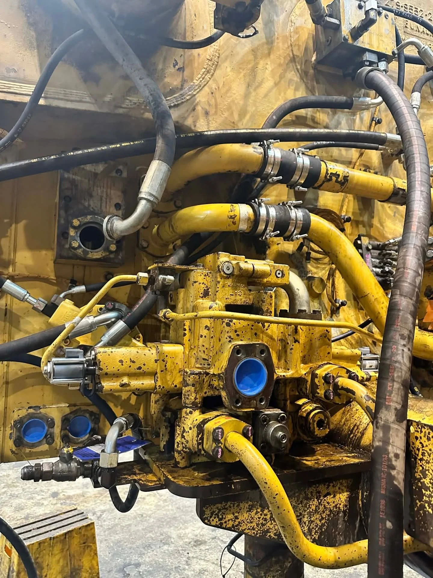Close-up of a yellow construction machine engine with various black and silver hydraulic hoses and fittings attached.