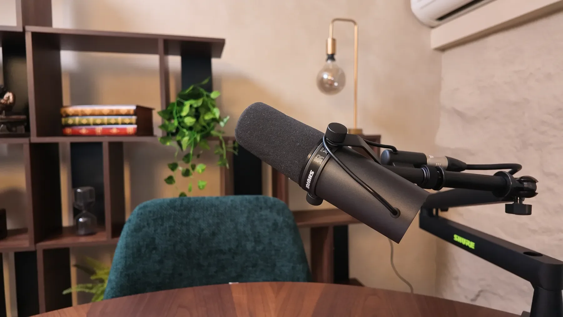 A podcasting microphone mounted on a boom arm  at Studio Analogue, Singapore Boutique Podcast and vodcast recording studio, with a bookshelf, plant, and lamp in the background.