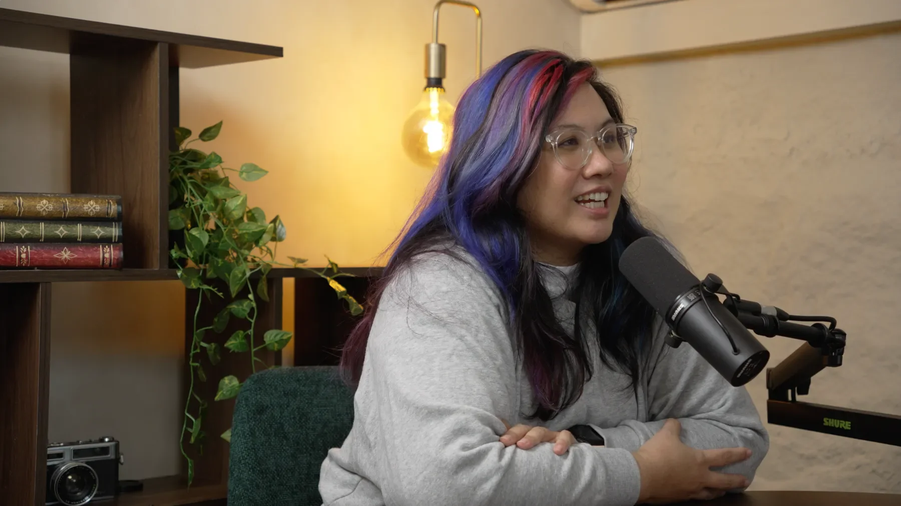 A woman with rainbow-colored hair is sitting at a desk with a microphone in front of her at Studio Analogue, Singapore Boutique Podcast and vodcast recording studio.