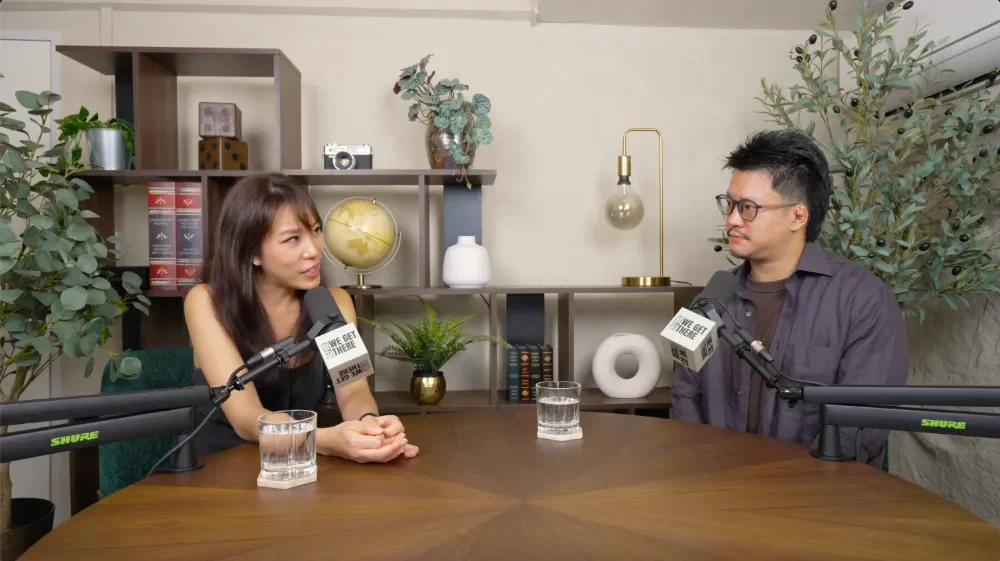 A man and a woman  sitting at a table with microphones, glasses of water, papers, and a tablet, recording a podcast at Studio Analogue. 