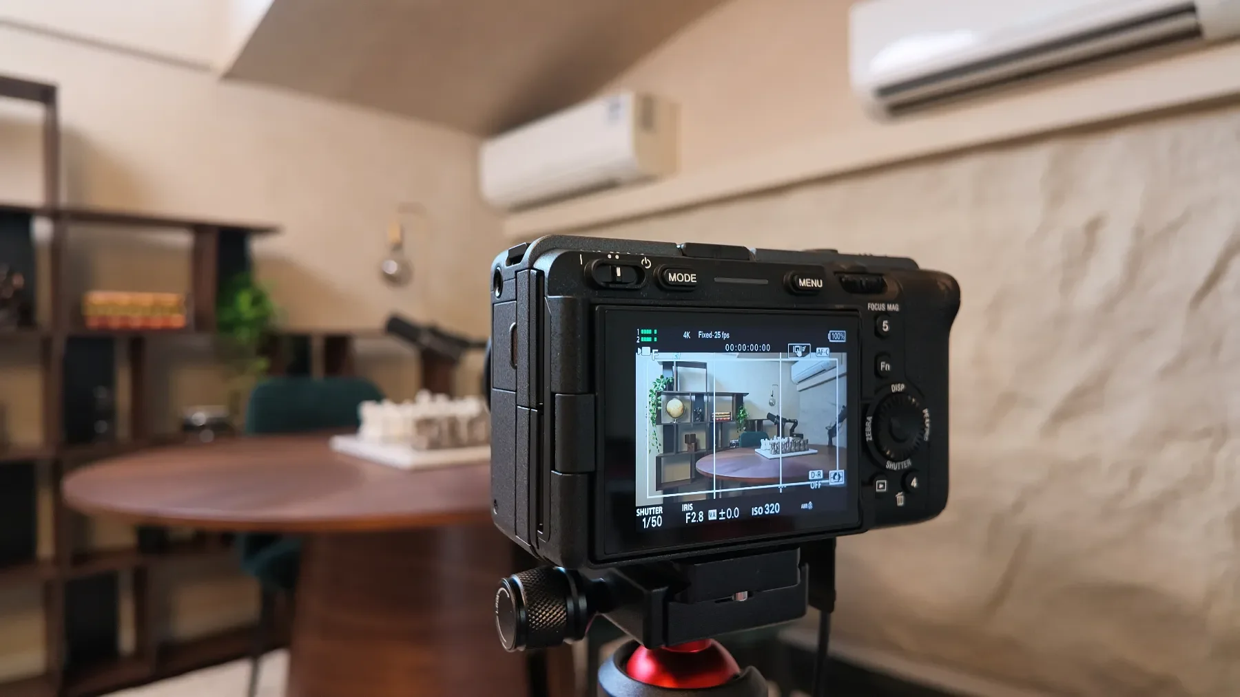 A camera capturing an indoor scene with a round wooden table, a green chair, a bookshelf, and air conditioners on the wall at Studio Analogue, Singapore Boutique Podcast and vodcast recording studio