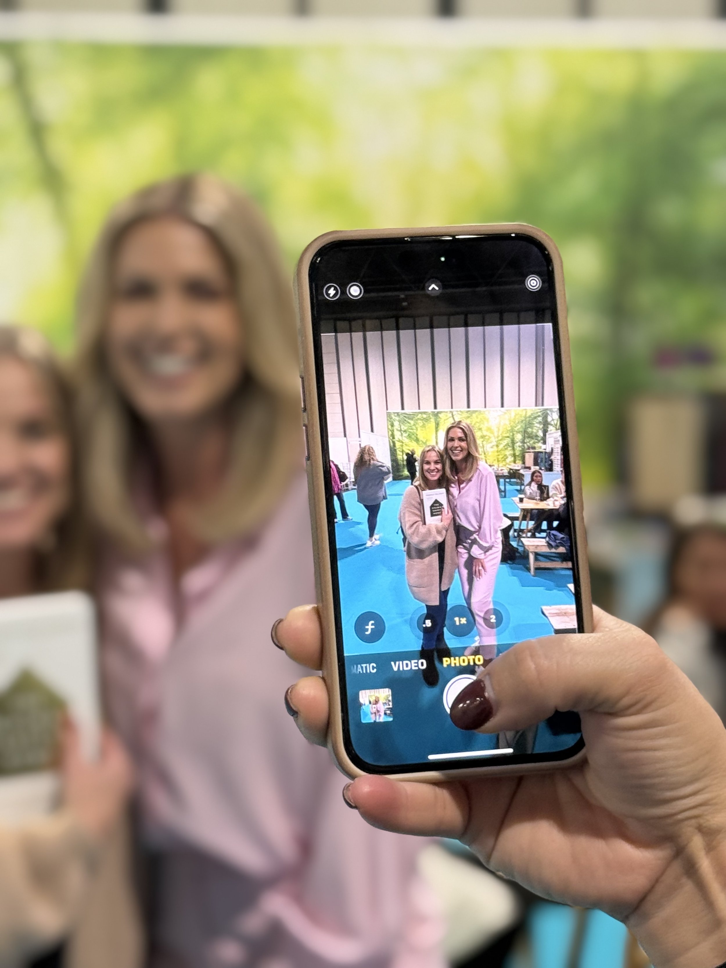 Person holding a smartphone taking a photo of two women smiling and posing at an event.