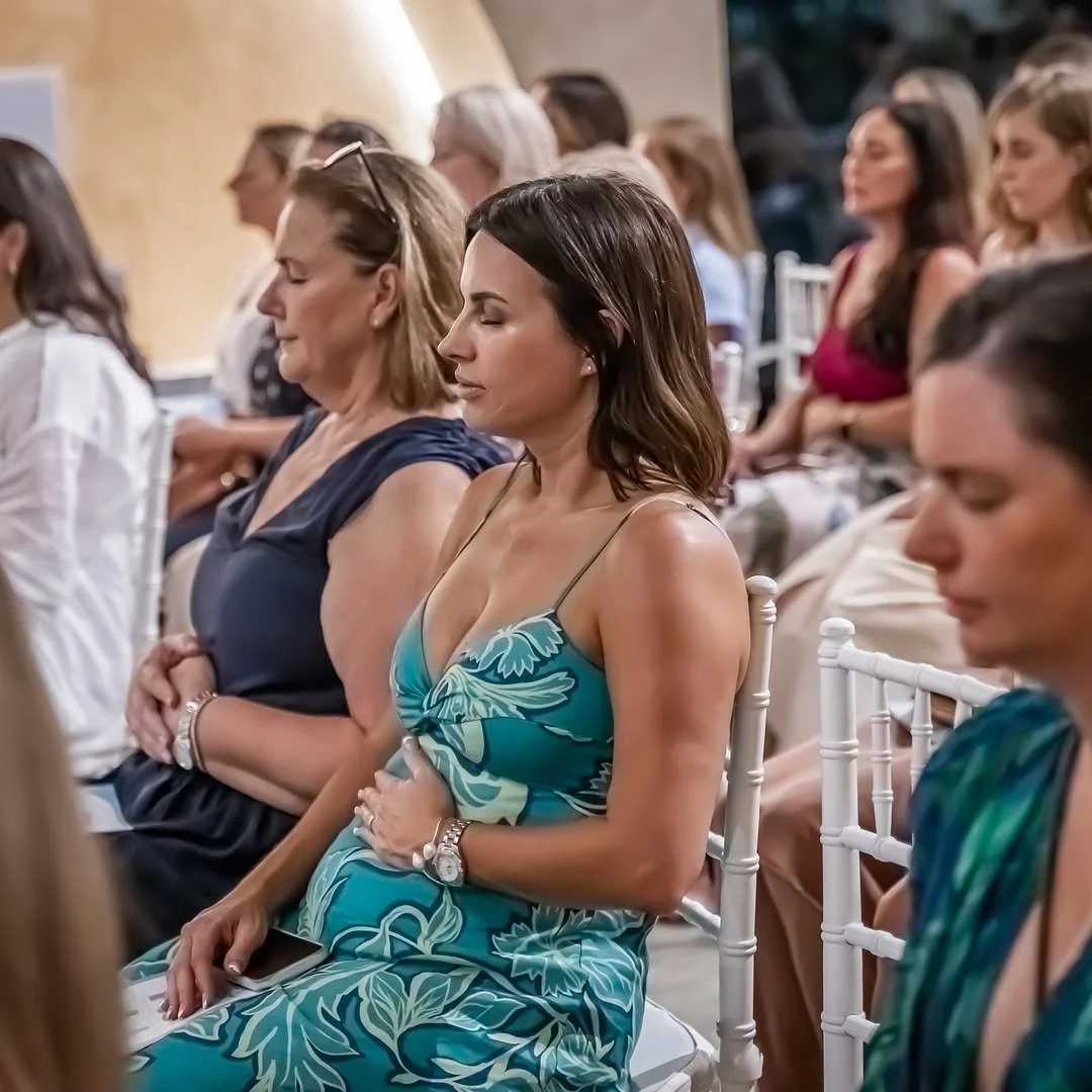 Women sitting with eyes closed at a formal event.