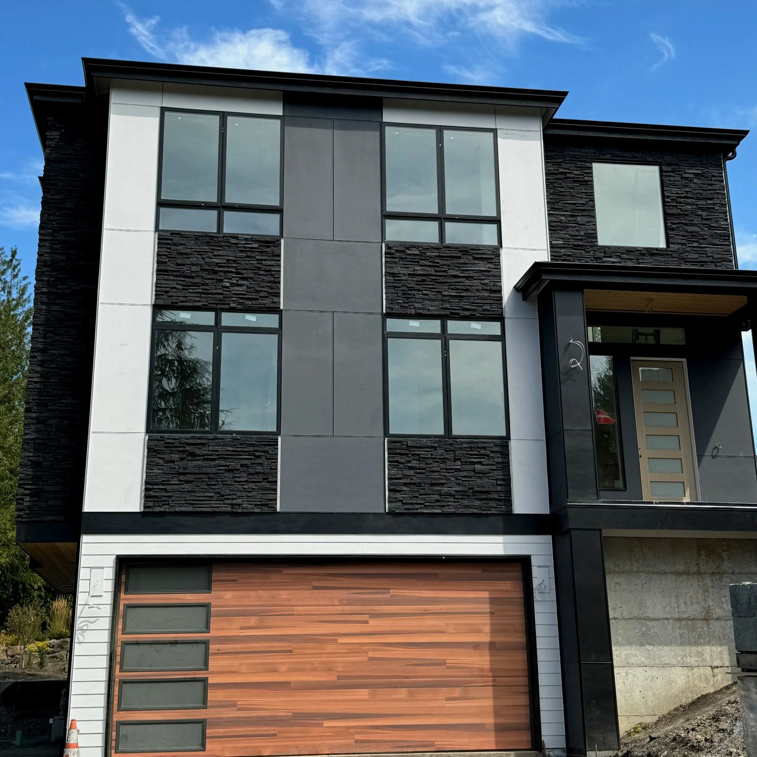 Modern multi-story house with large windows, black and white exterior, and wooden accents, under a cloudy blue sky.