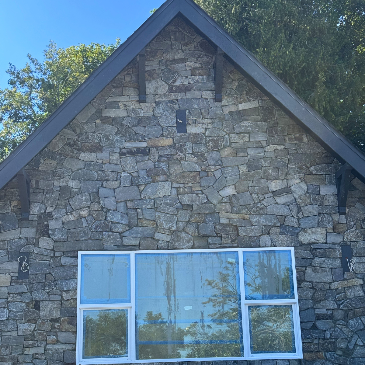 Front view of a house with a stone exterior, large windows, and a steeply pitched roof.