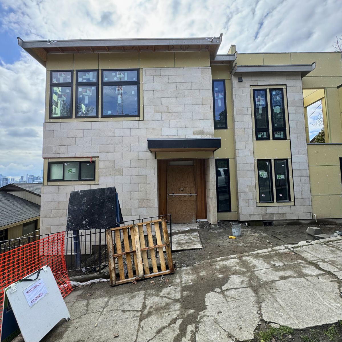 Under construction multi-story residential building with new windows, partially finished exterior walls, construction materials, and a sidewalk closed sign in the foreground.