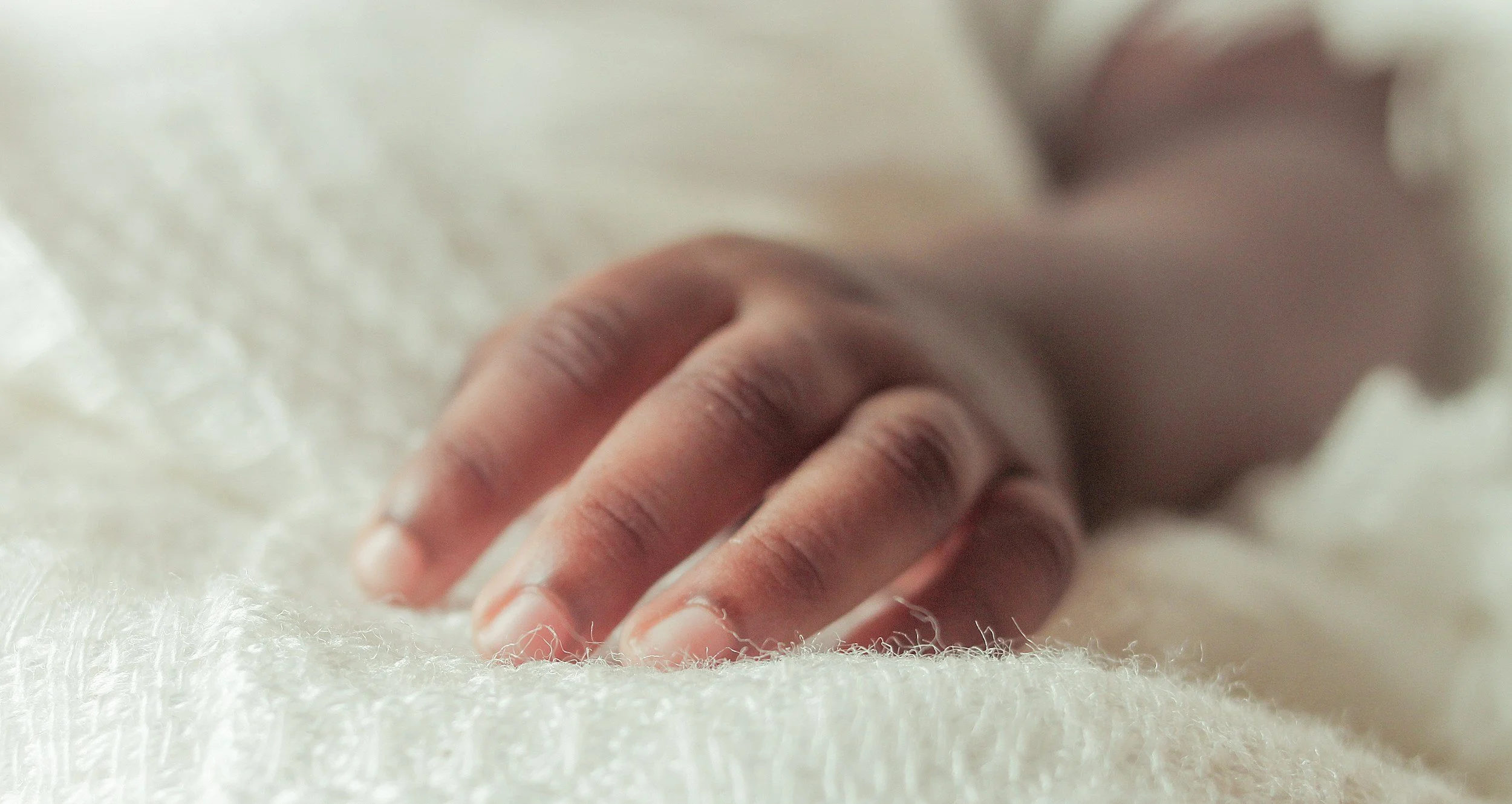 Close-up of a baby's hand resting on a soft white blanket.
