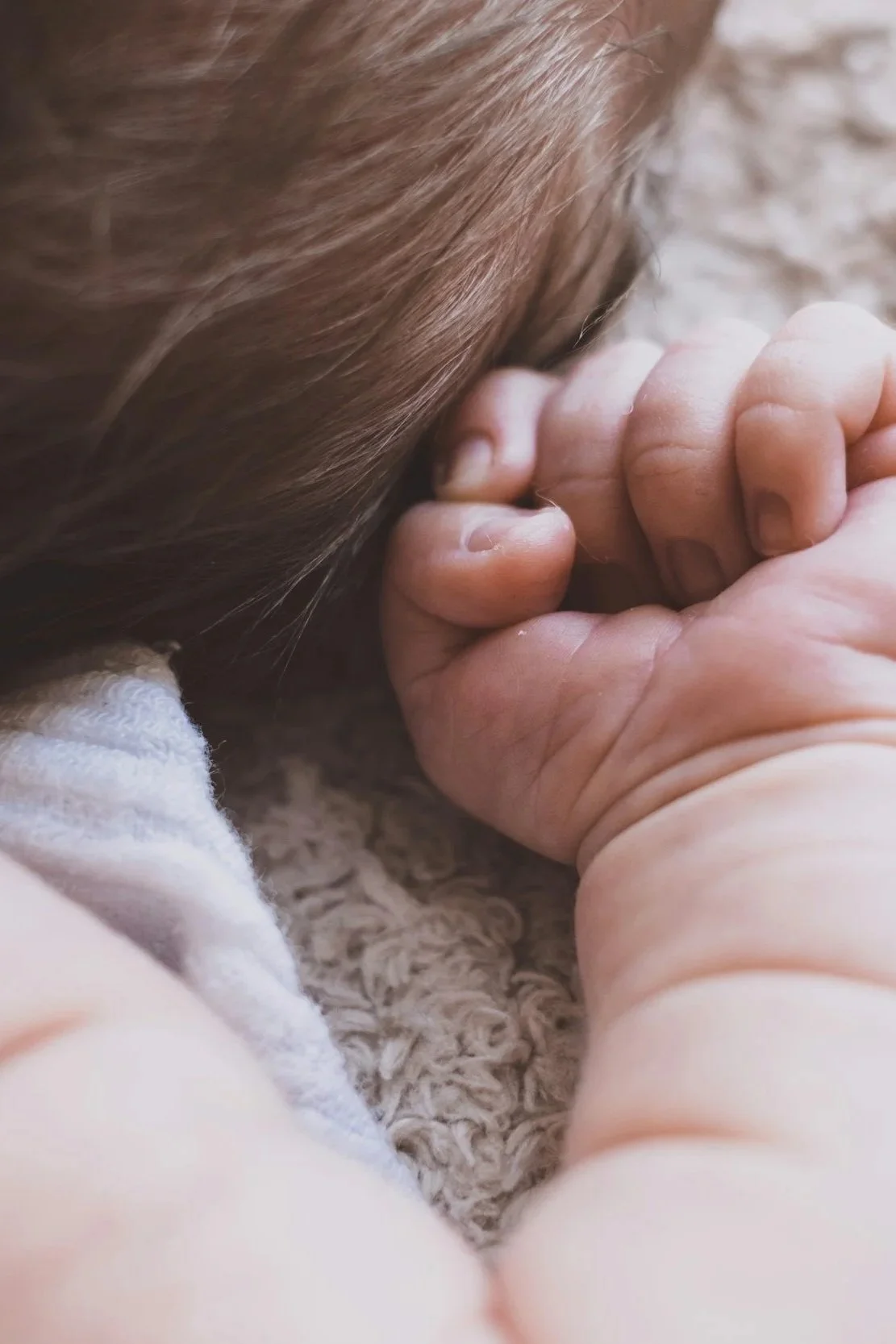 Close-up of a child's head and hand, with the child's head resting on a soft textured surface and hand gently holding their lips as they sleep peacefully
.