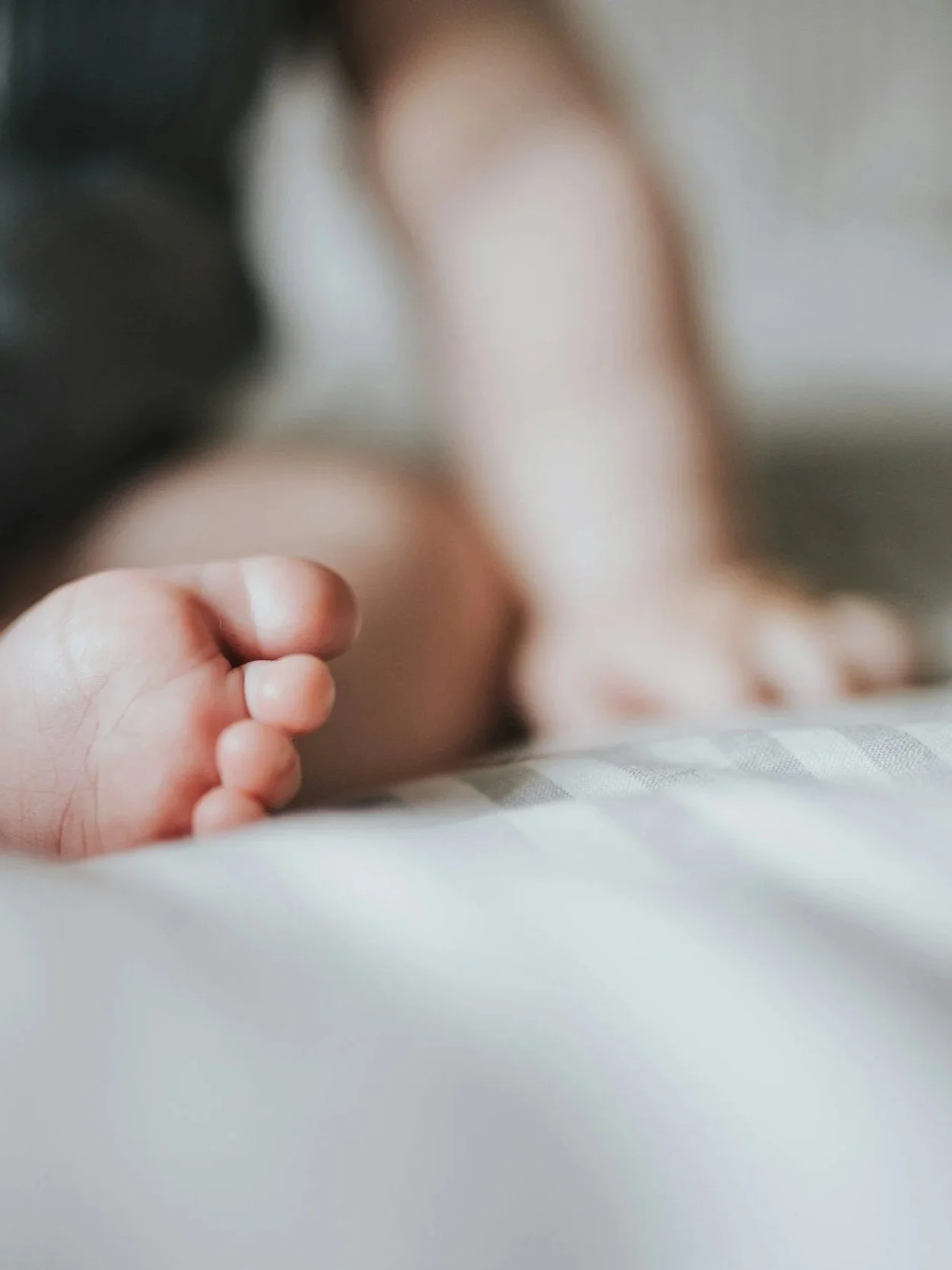 Close-up of a baby's tiny foot with curled toes, lying on a soft surface, with a blurred background.