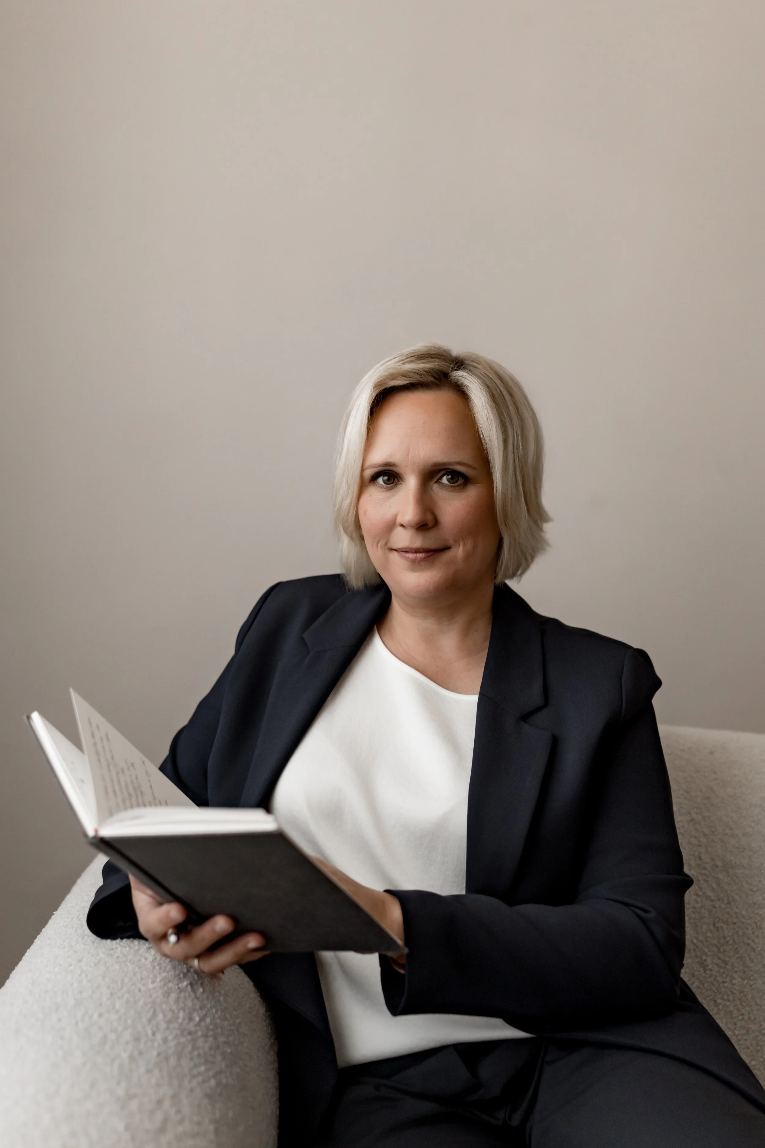 Monique Fordt, psychologische Beraterin für Unternehmensnachfolge, sitzt mit einem Buch auf einer hellen Couch