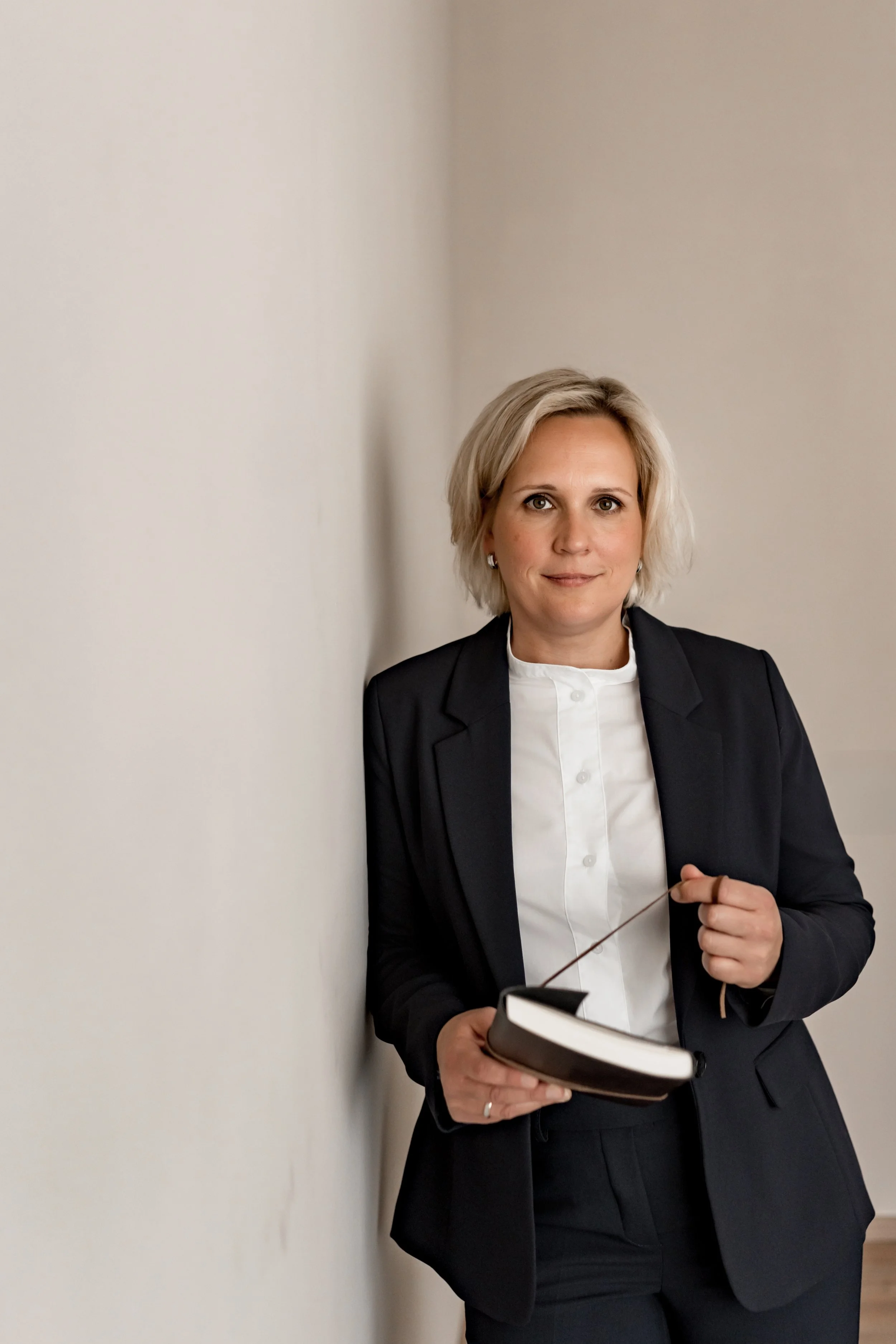 Monique Fordt steht mit Notizbuch an einer Wand — bereit für die Zusammenarbeit