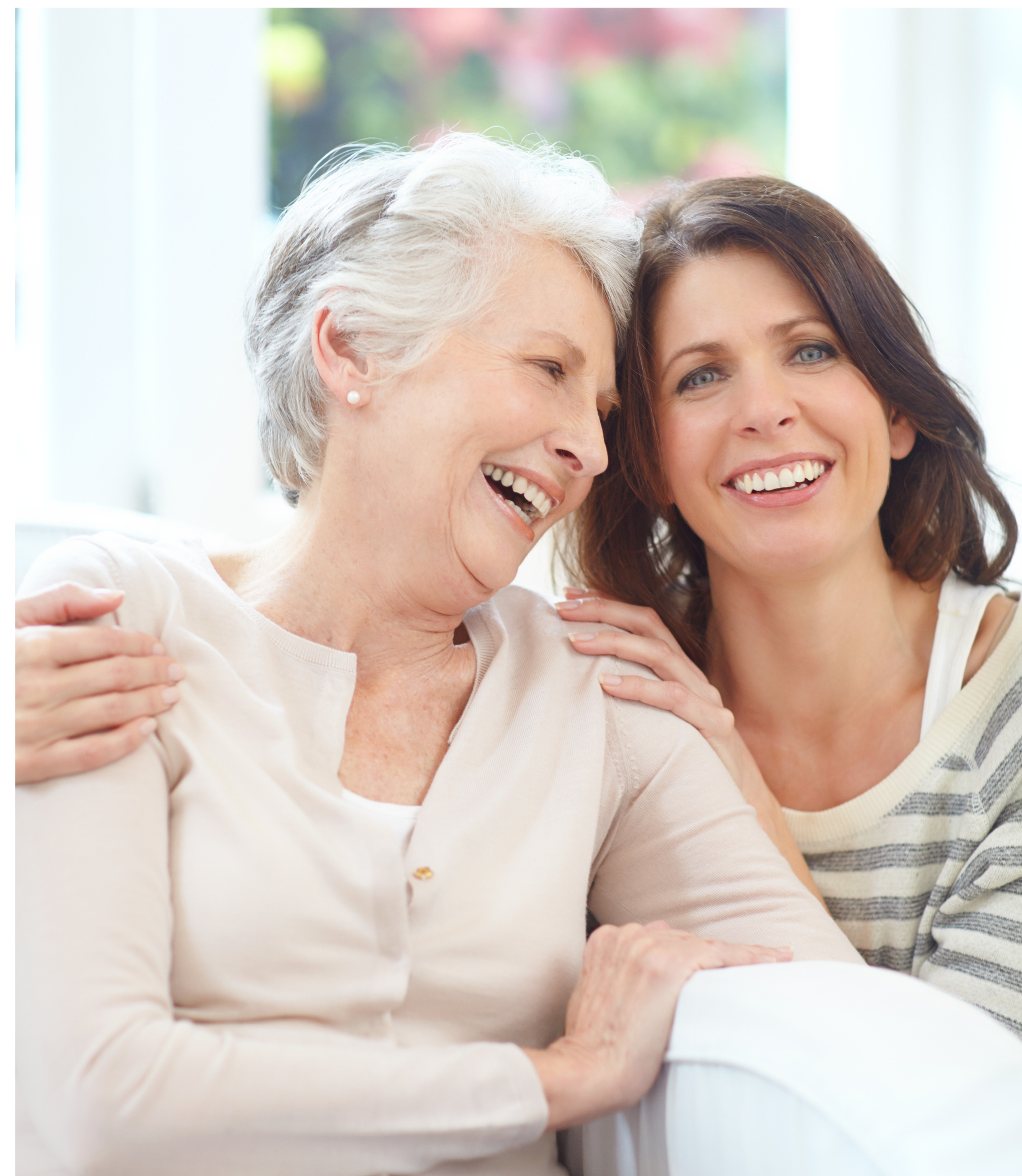 Two women, one elderly with white hair and pearl earrings, and one younger with brown hair and blue eyes, smiling and hugging each other.