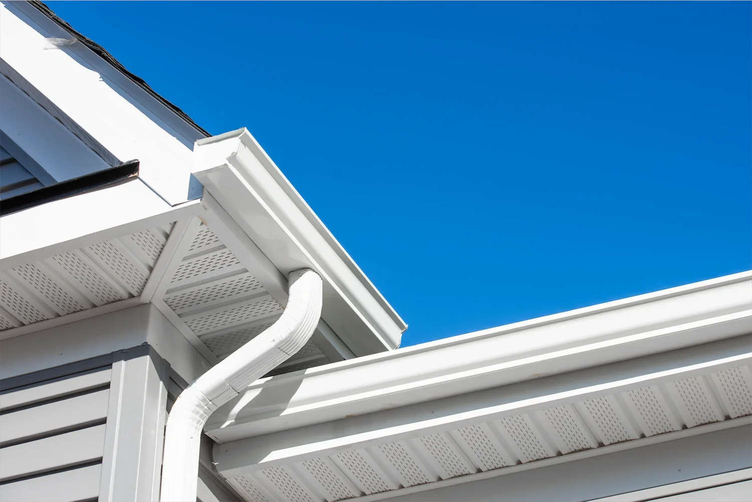 Close-up of the white gutters and roofline of a modern house against a clear blue sky.