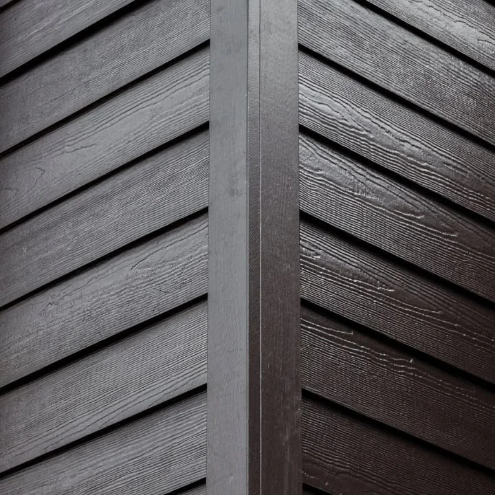 Close-up of dark brown wooden exterior siding with vertical trim at the junction.