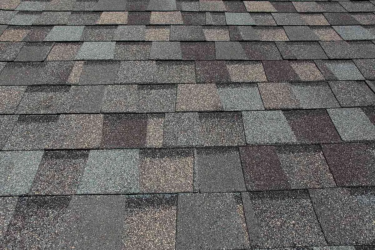 A close-up of a section of a roof with asphalt shingles in various shades of gray, reddish brown, and black.