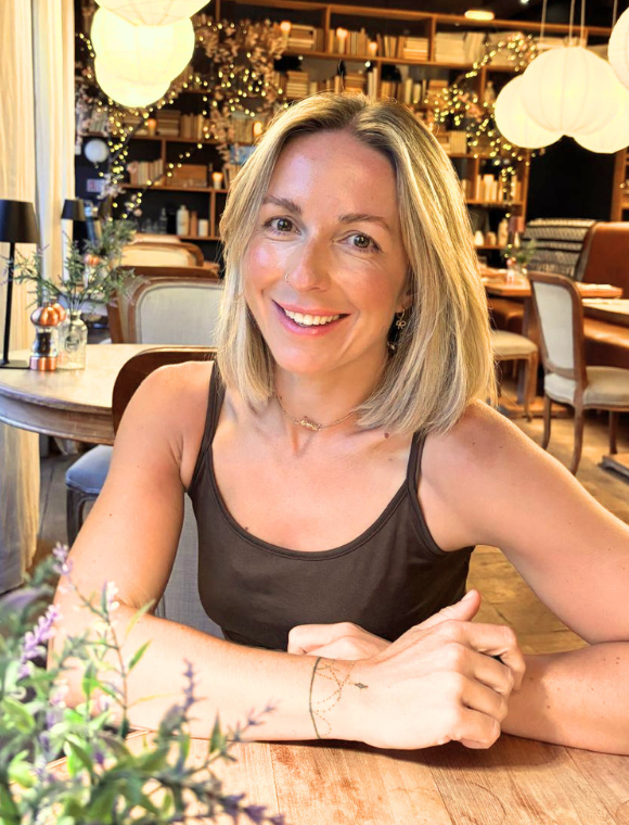 Instructor, Nico, with blonde hair and a black tank top sitting at a table in a cozy, decorated restaurant.