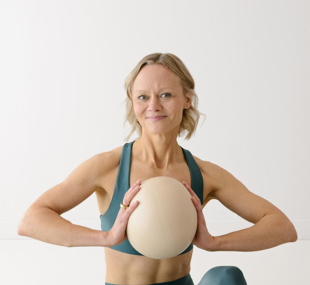 Instructor, Maija McKerrow, in workout attire holding a beige exercise ball.
