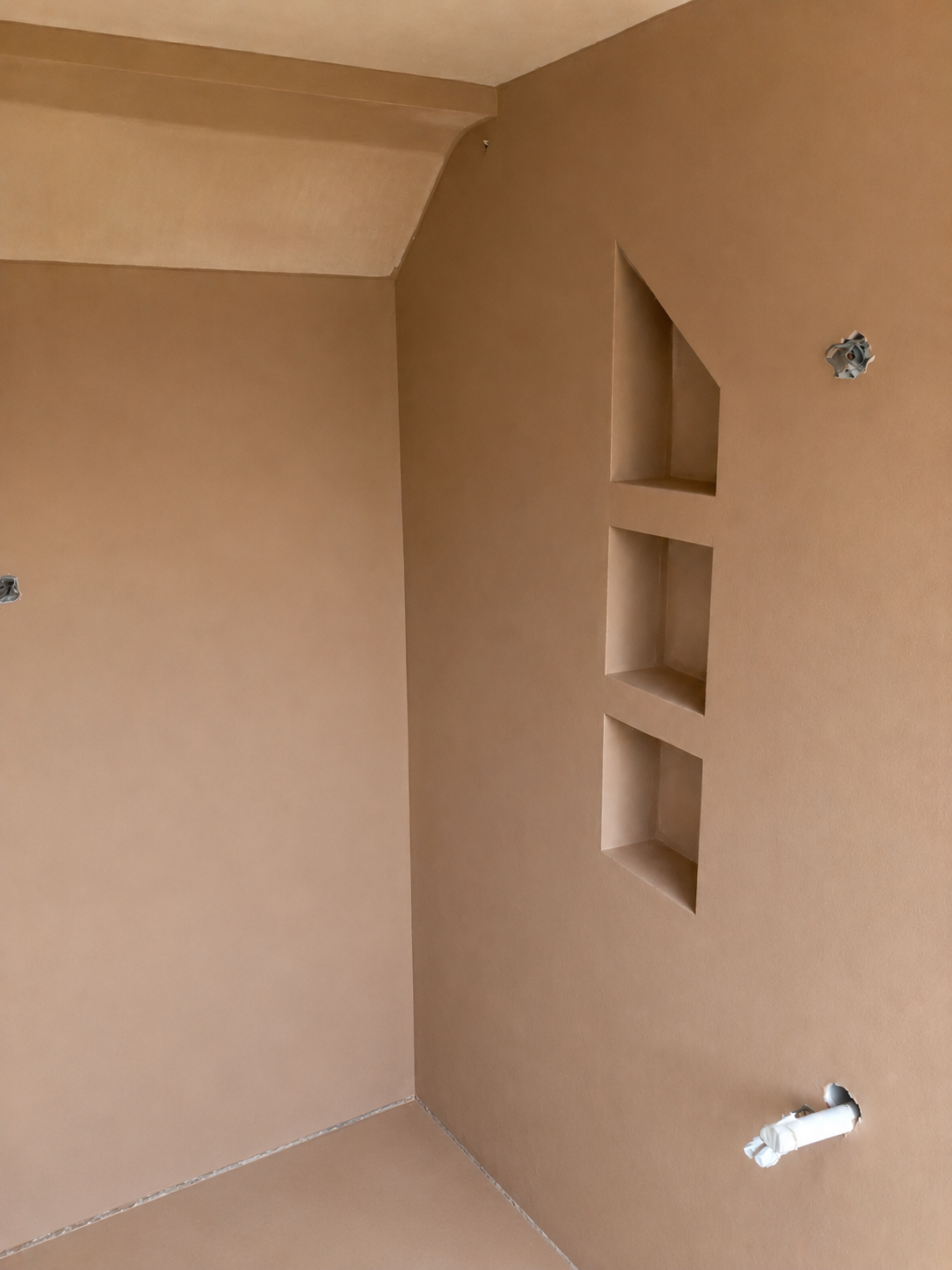 Interior of a beige cabinet with three built-in shelves and electrical outlets with wiring.