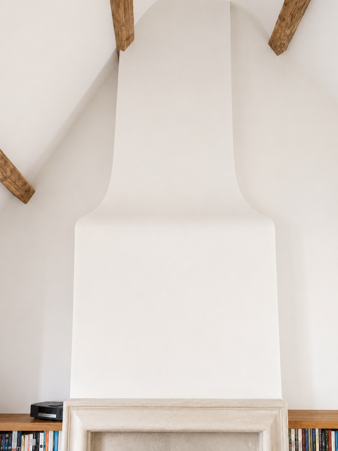 Interior view of a fireplace with a minimalist design, white wall, wooden beams, and built-in bookshelves at the bottom.