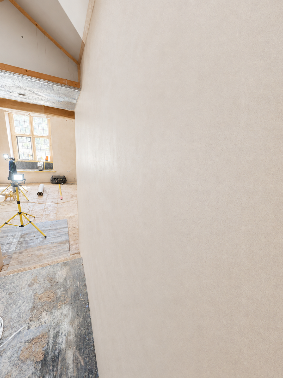 Interior of a room under renovation with construction tools, a ladder, and a large window, partially obscured by a large empty wall.