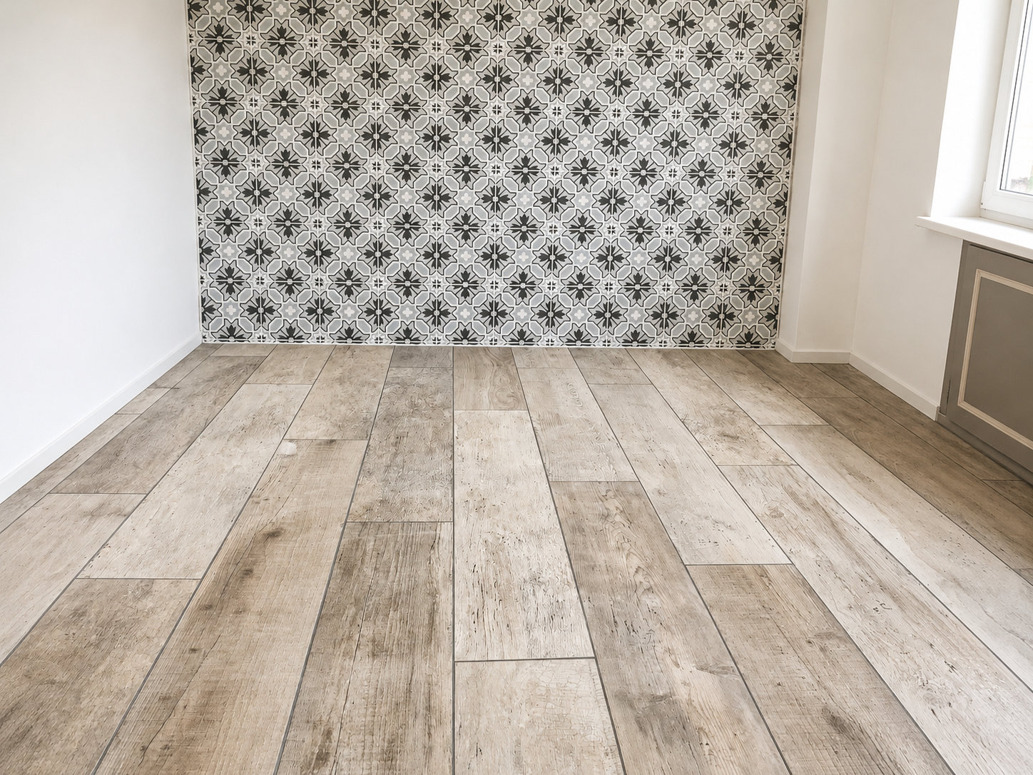 Empty room with patterned black and white tile accent wall, light wood floor, white walls, and a window on the right side.