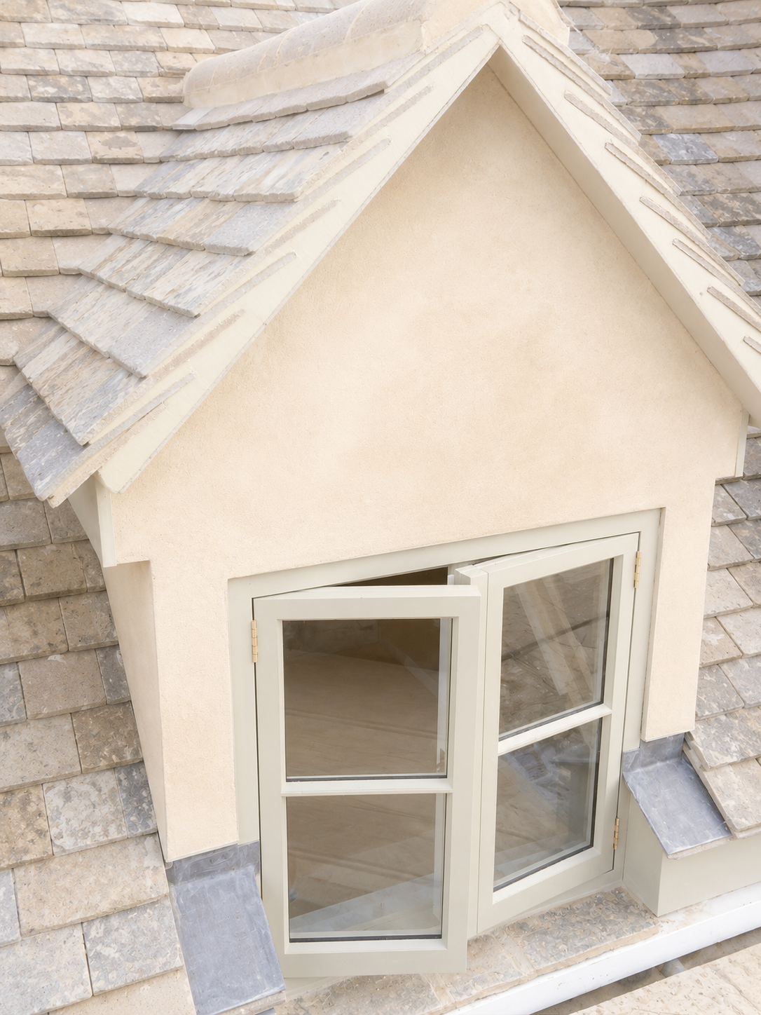 Close-up of a beige house with a gable roof, covered in tan and gray shingles, and a window with a white frame and open double panes.