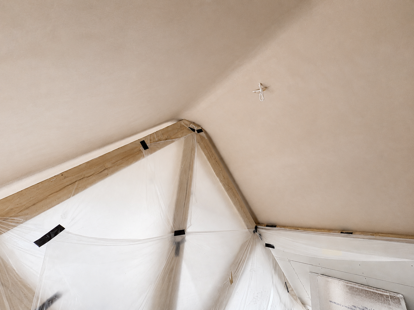 Corner of a room with a sloped ceiling, paint, and a plastic sheet taped to the wall for protection.