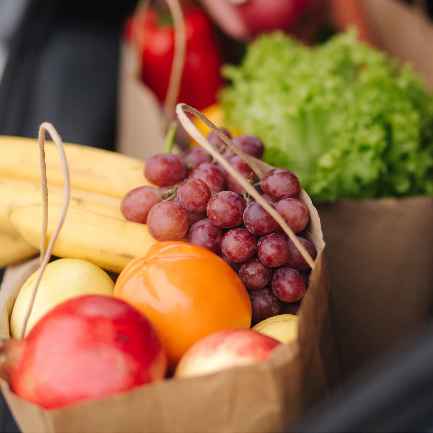 Close-up of a basket filled with red grapes, oranges, yellow lemons, and apples, viewed from the side.