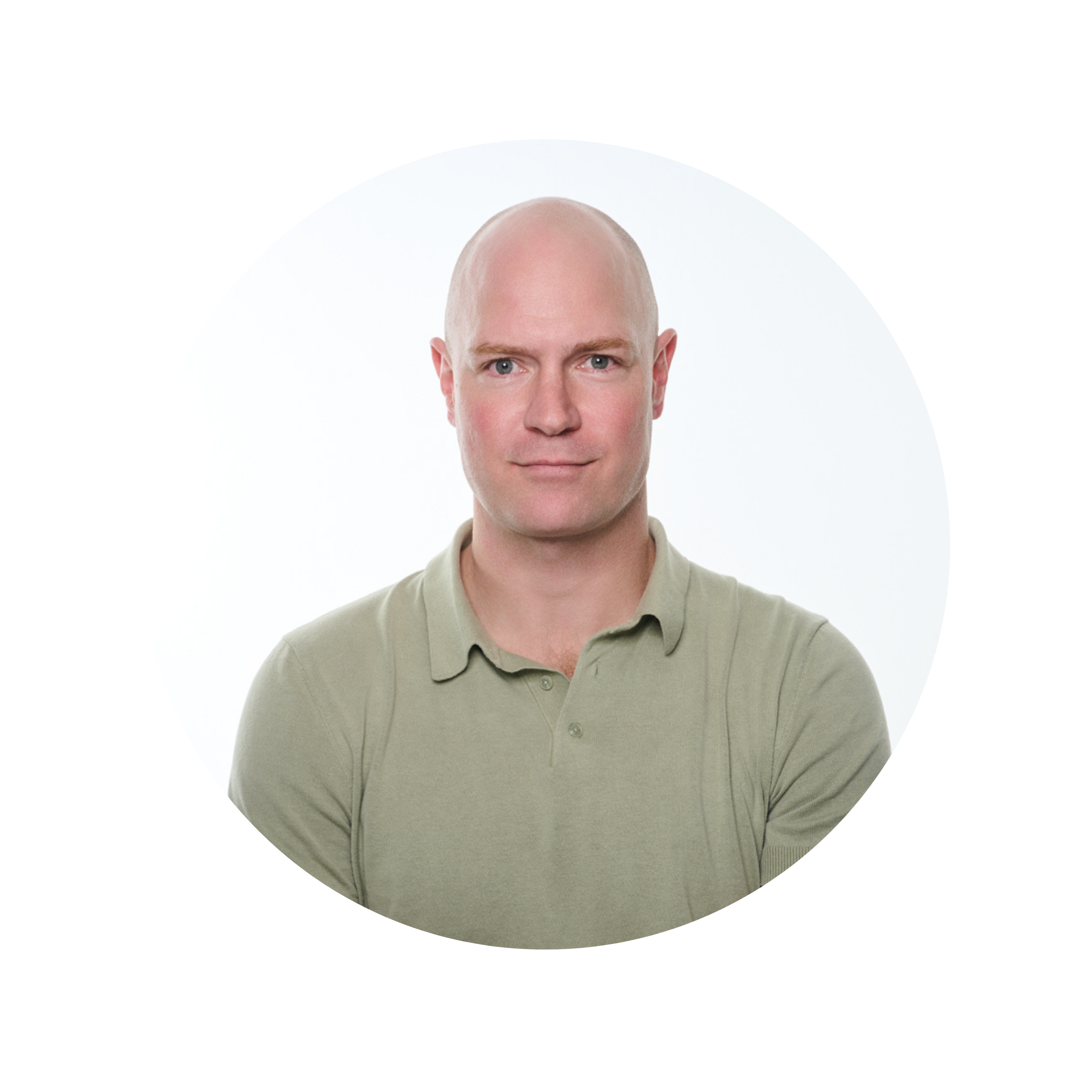Close-up of a bald man with blue eyes, wearing a light gray polo shirt, looking directly at the camera, with a white background.