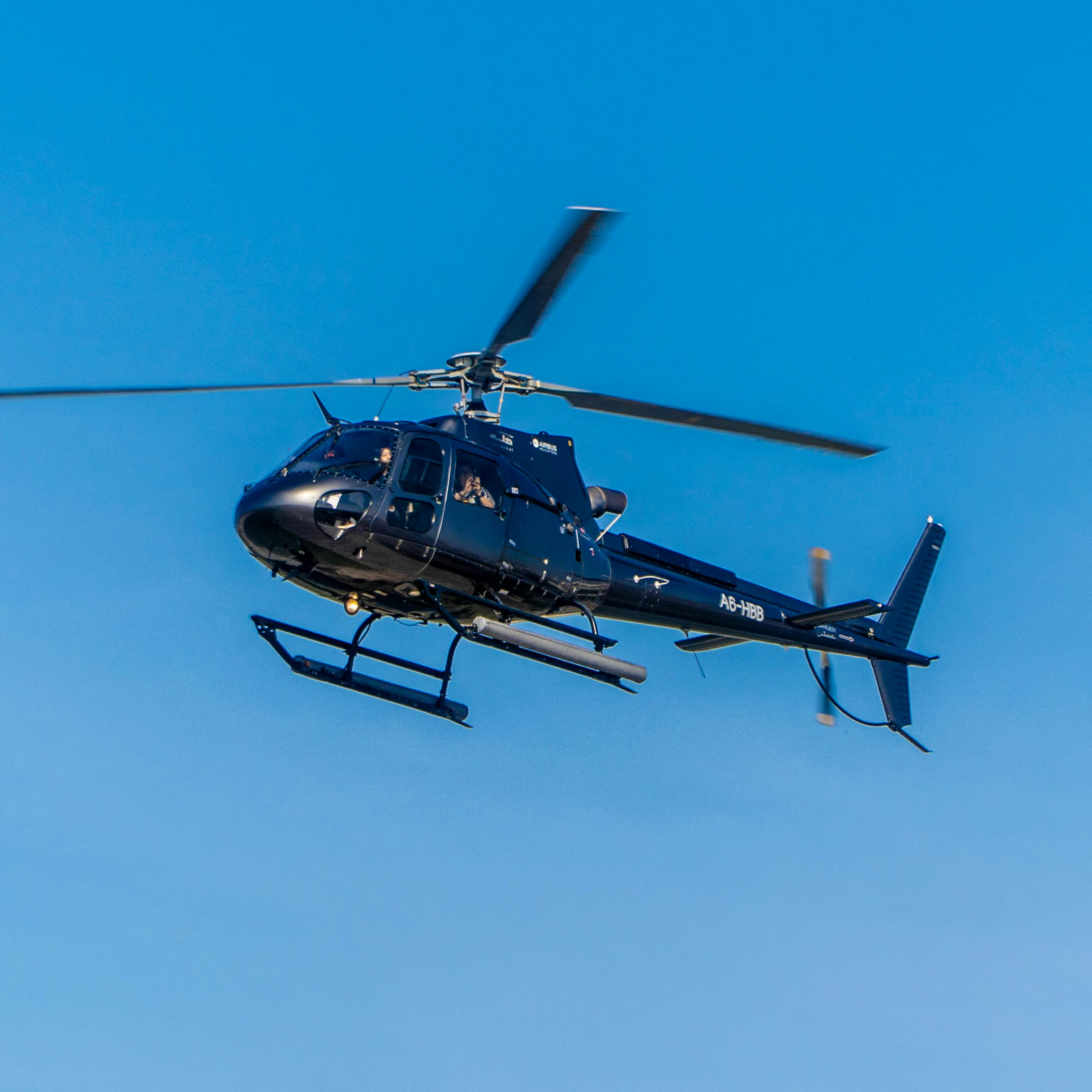 A black helicopter flying against a clear blue sky.