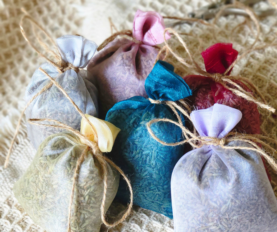 Six mixed coloured organza bags, filled with lavender seeds, tied with twine and resting on a textured surface.