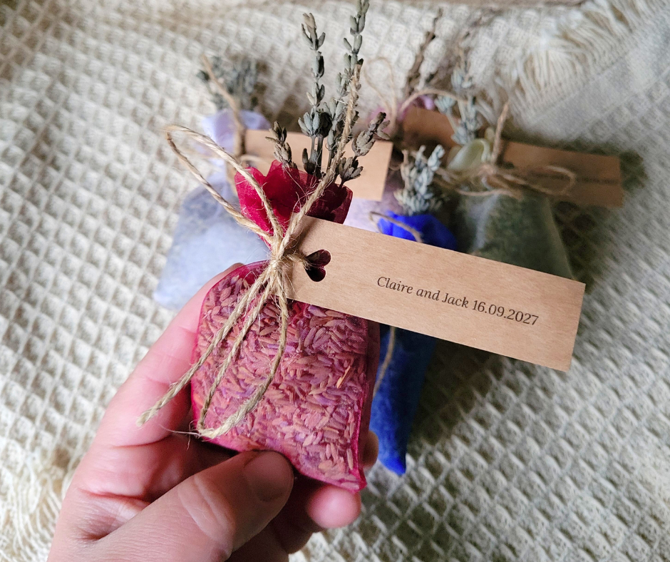 A hand holding a red organza bag filled with dried lavender with a brown tag that reads "Claire and Jack 16.09.2027."