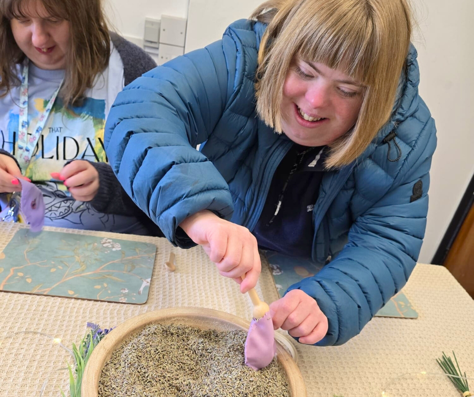 Young woman with blonde bob and blue puffer coat is filling an organza bag with dried lavender