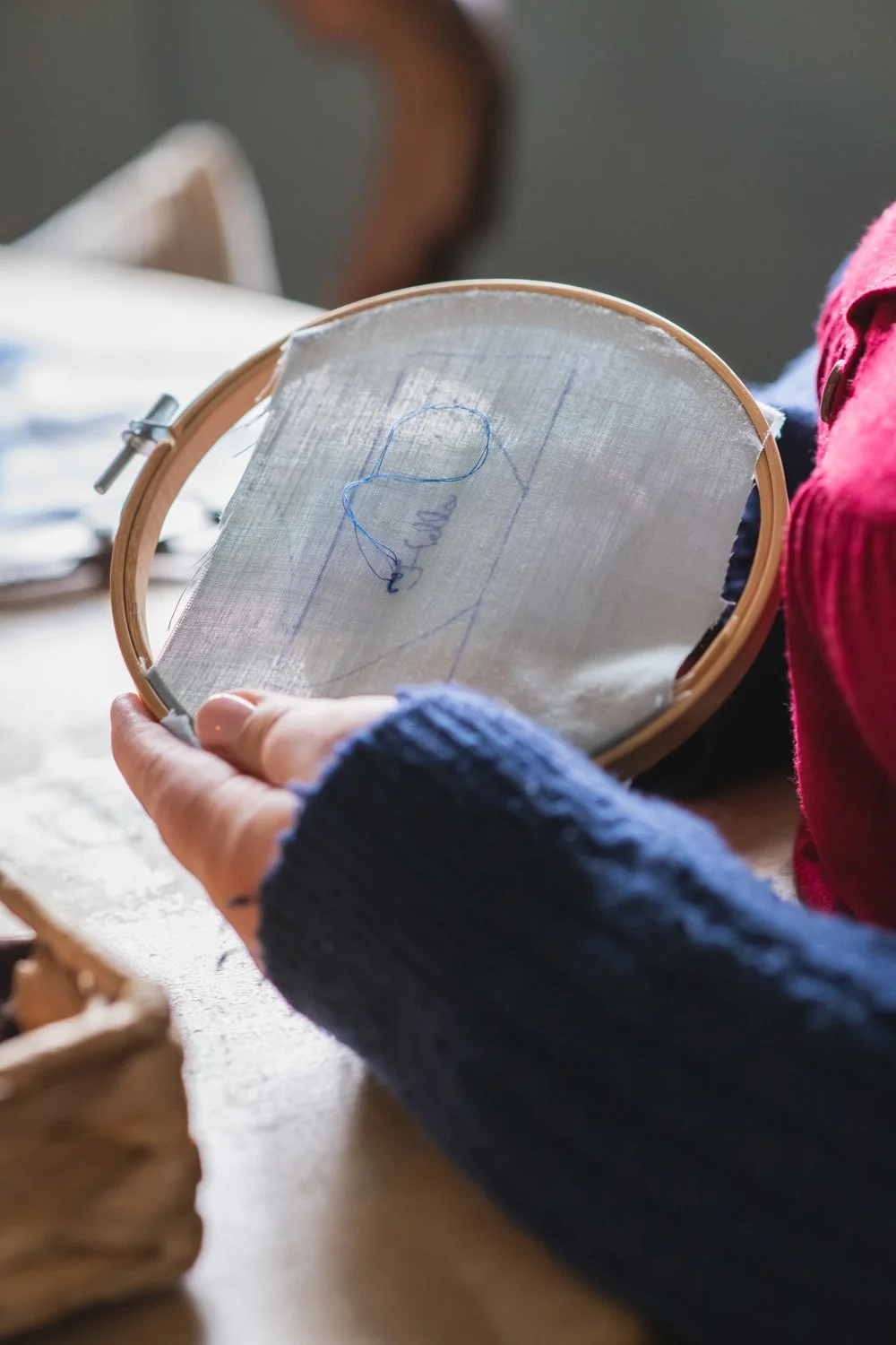 Person holding an embroidery hoop with fabric showing blue thread and sketches.