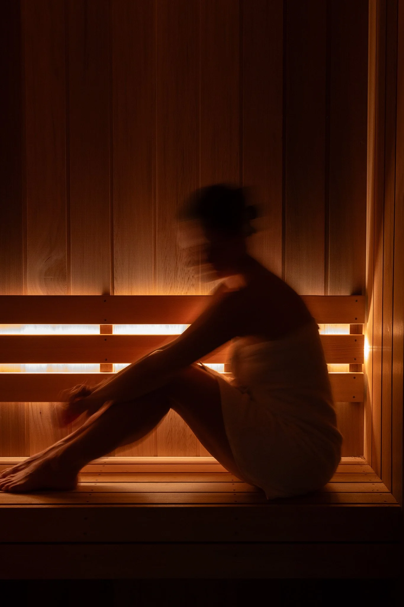 Person in a seated yoga pose at koko studio inside a wooden sauna, with warm backlighting and vertical wooden panels on the walls. Located at Erina, Central Coast.