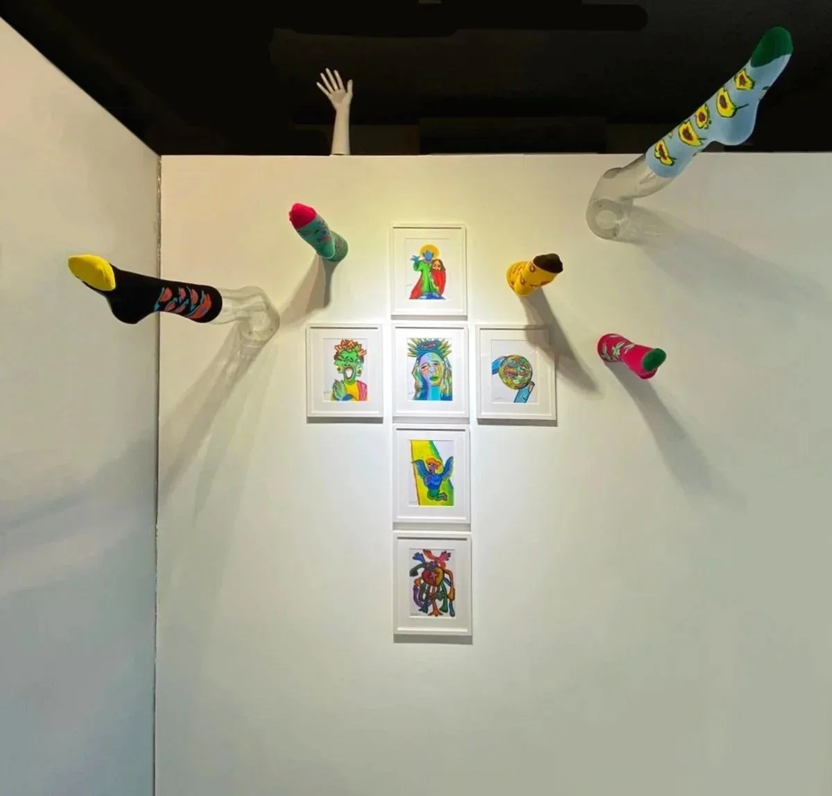A wall of displaying six oil pastel painting with white wood frame, set-up with certain fake legs and vivid colour patten socks