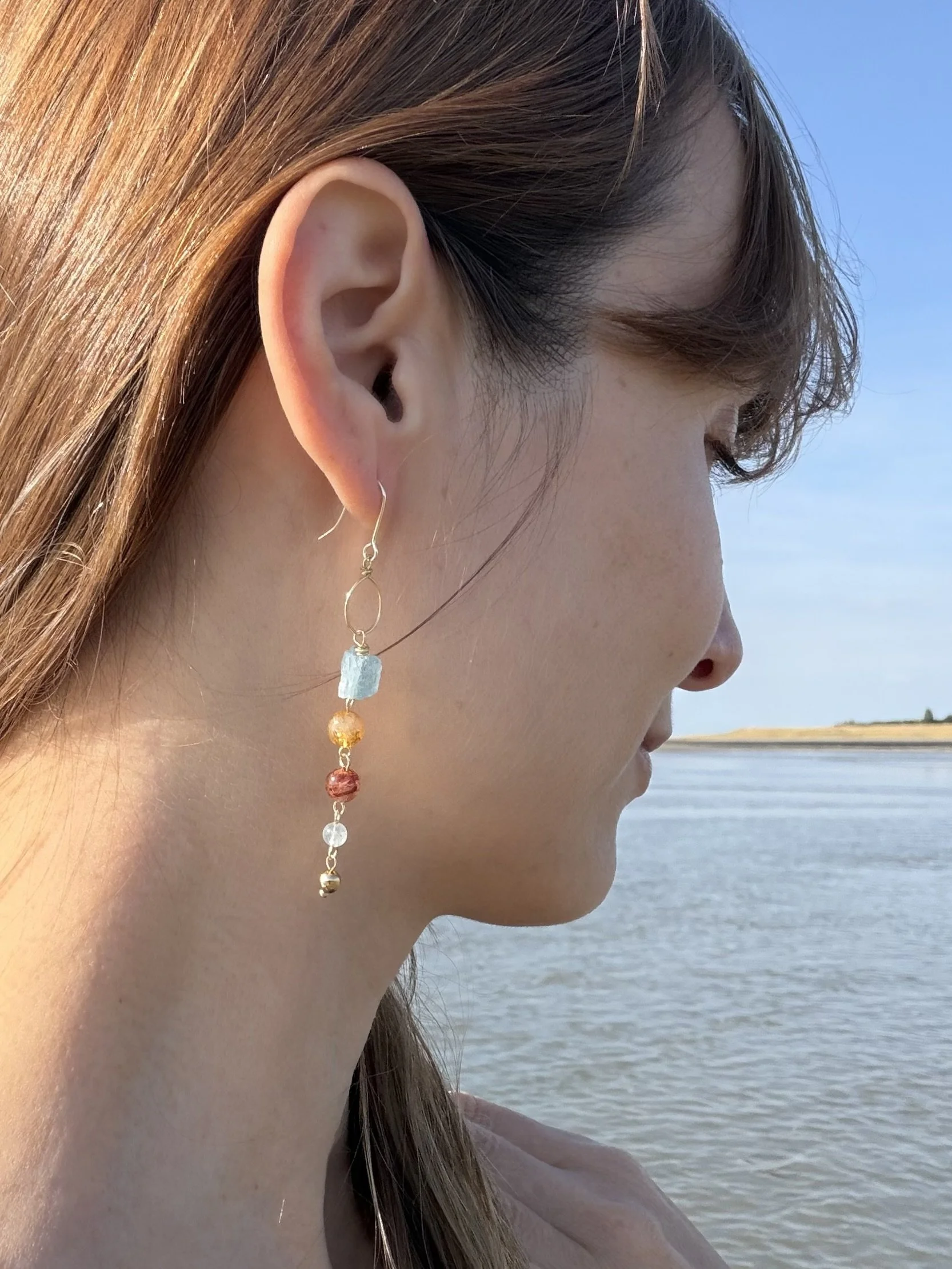 Handmade gemstone drop earring worn by the sea, showing the length and delicate dangling design.
