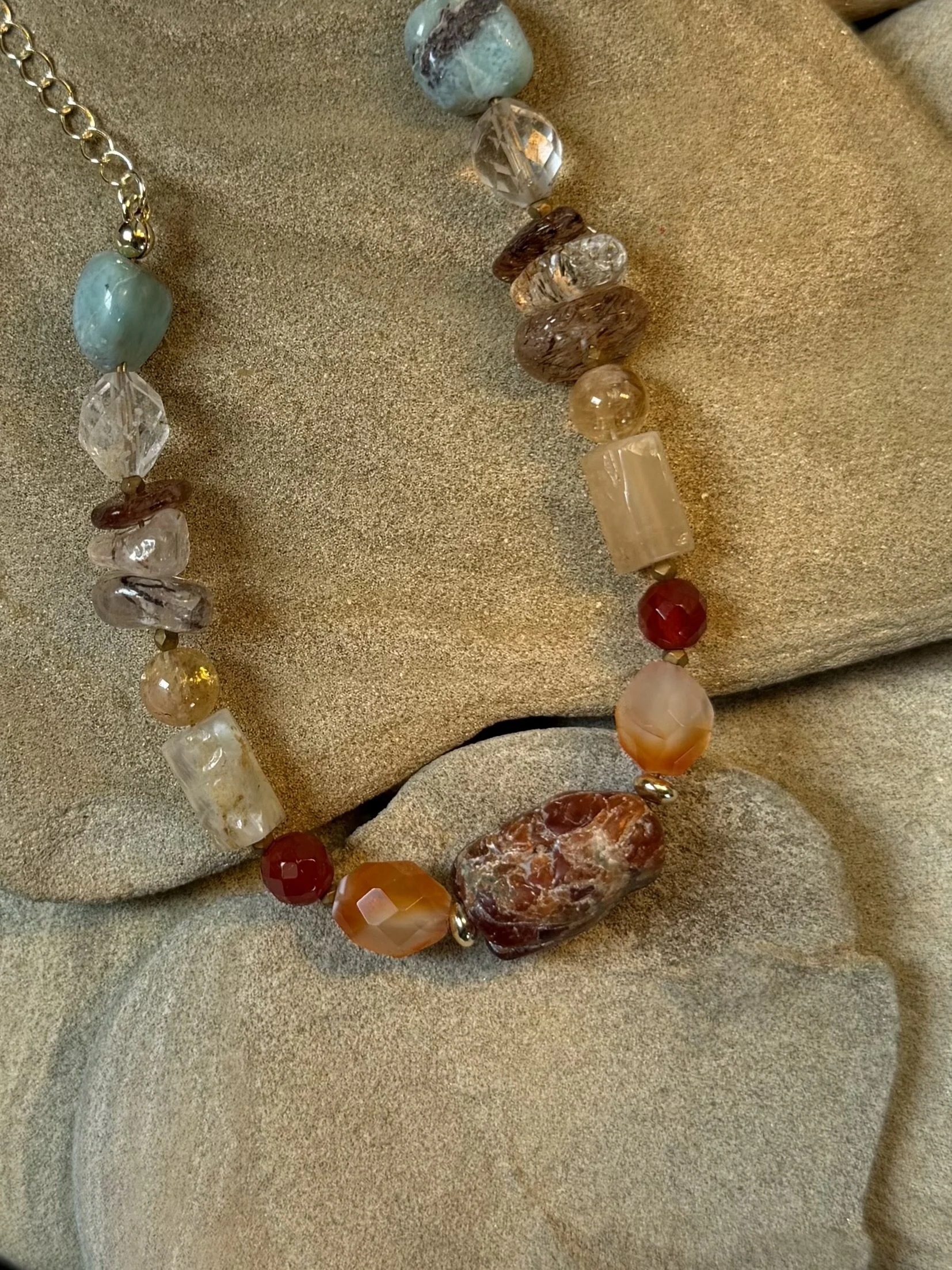 Close-up of a handmade necklace featuring a colourful mix of natural gemstones in blue, red, amber and earthy tones.
