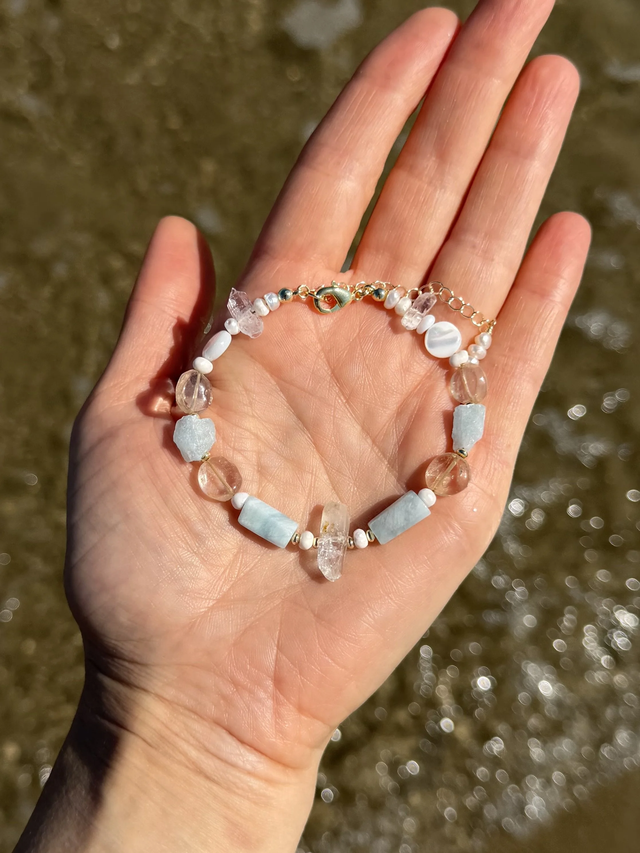 Close-up of a handmade gemstone bracelet with pale blue, white and translucent stones resting in a hand.