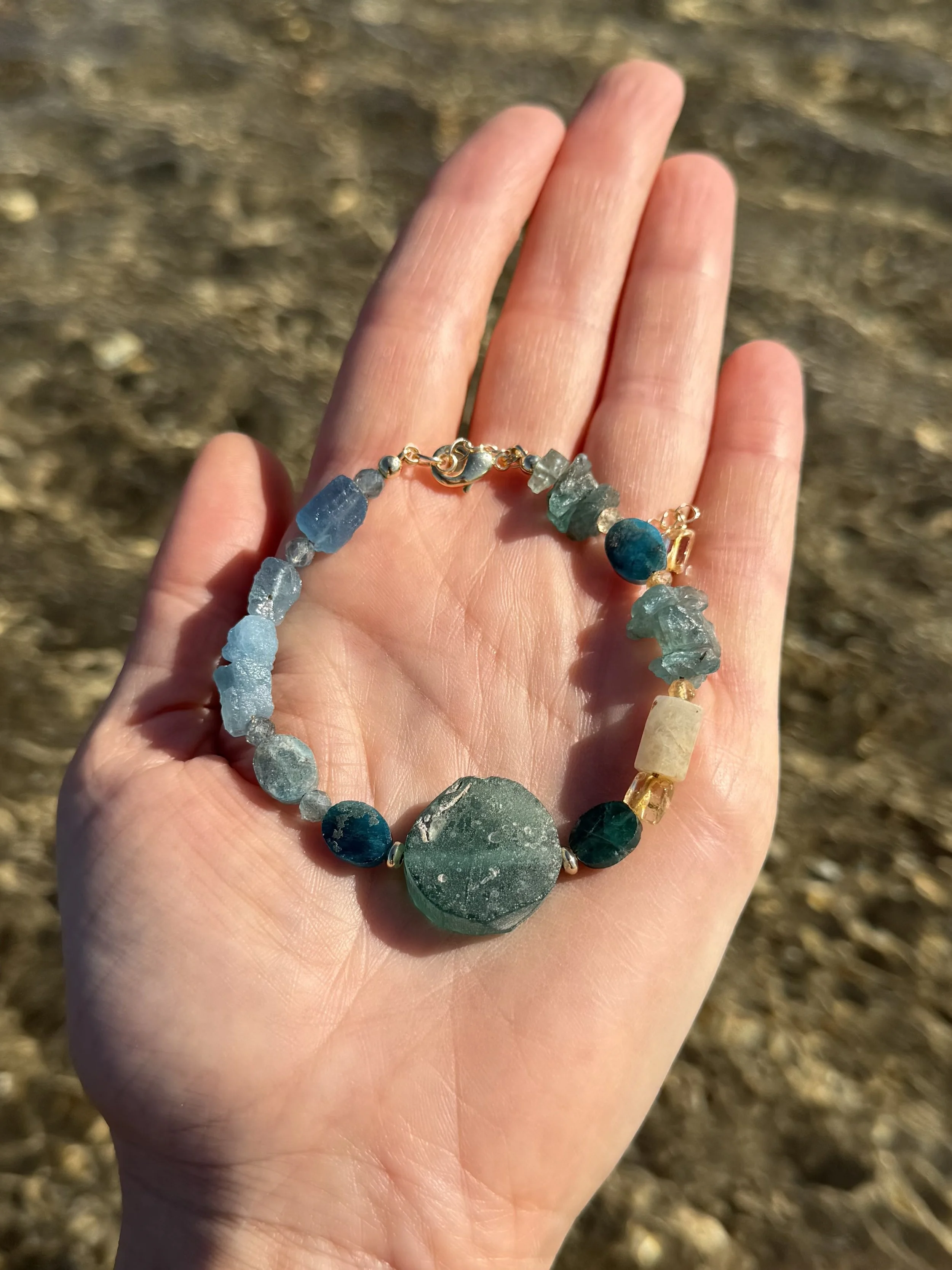 Handmade gemstone bracelet with green, turquoise and pale stones displayed in a hand.