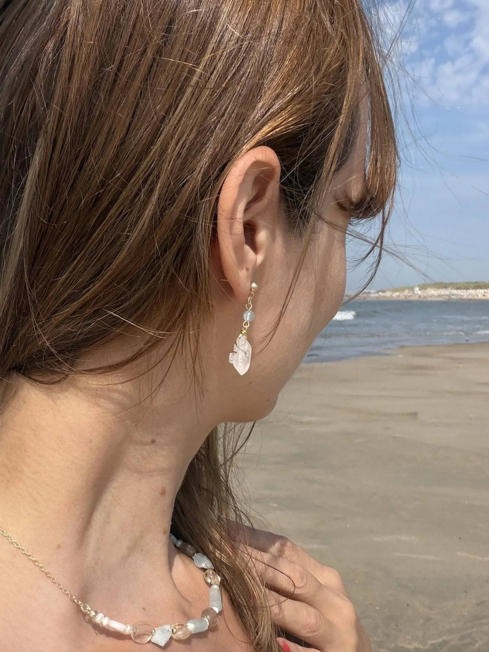 Handmade gemstone drop earrings with translucent stones worn at the beach, showing their length and delicate design.