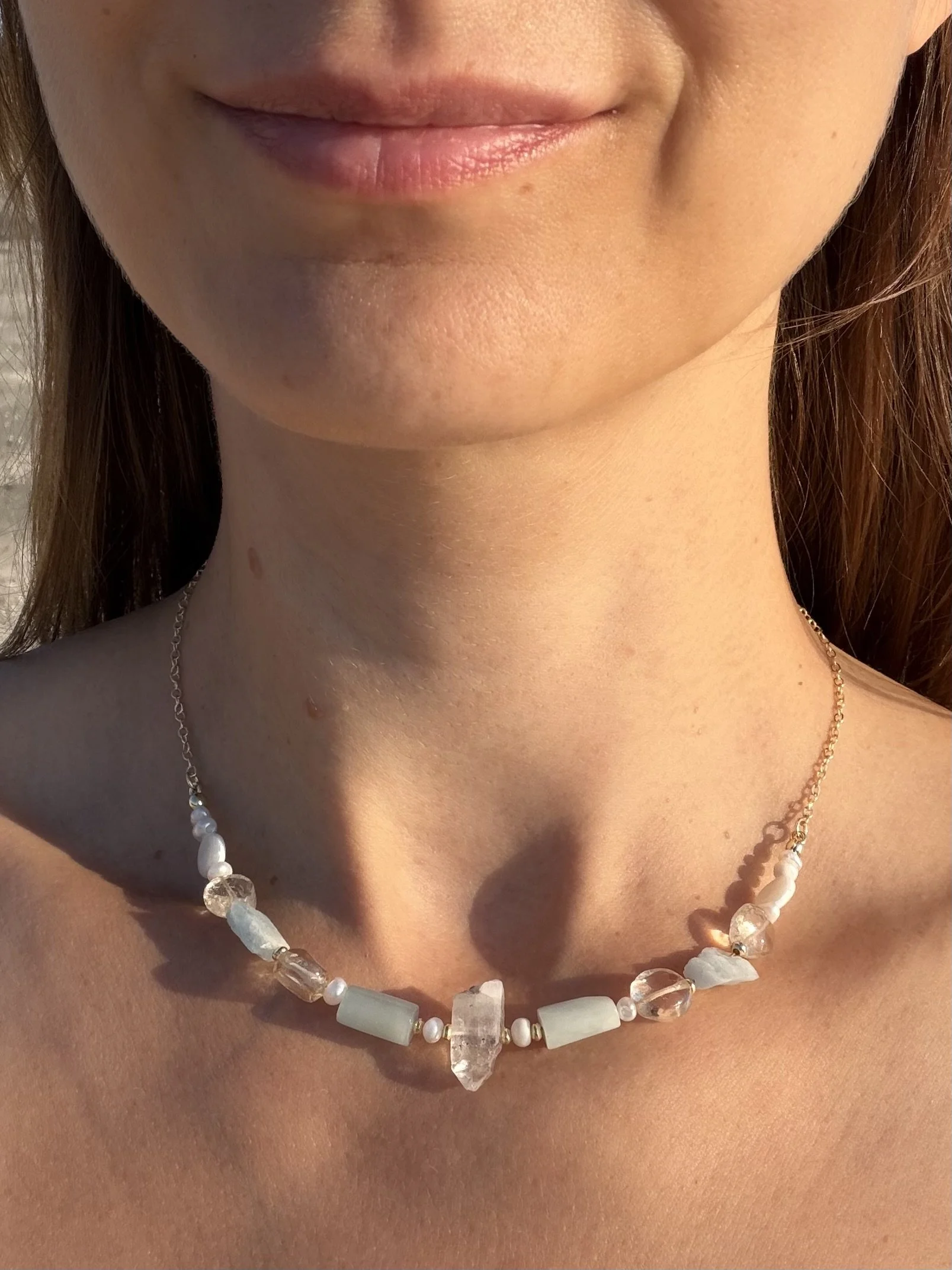 Handmade gemstone necklace with soft blue, white and translucent stones worn at the collarbone.
