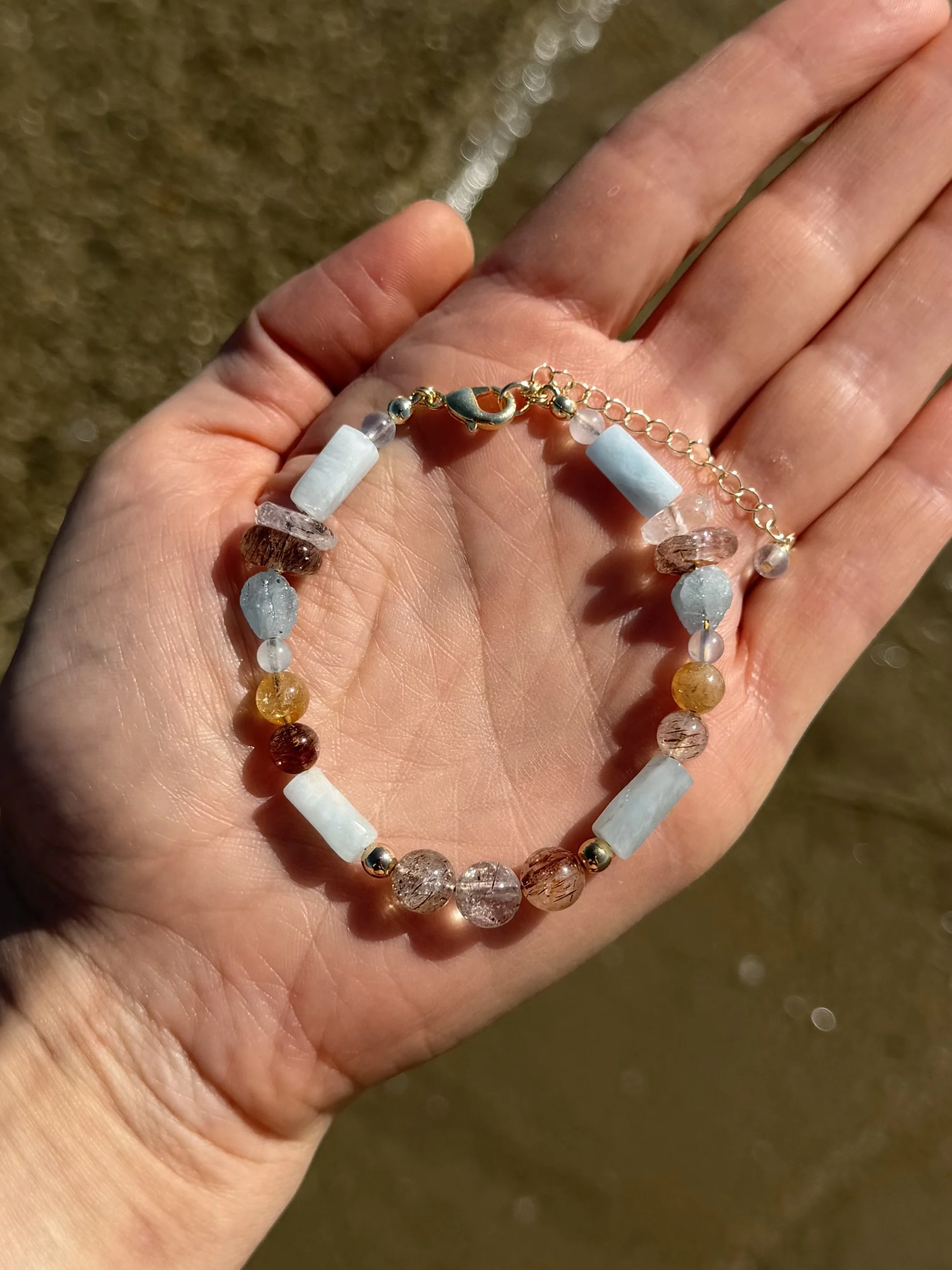 Close-up of a handmade gemstone bracelet with blue, white, pink and warm-toned natural gemstones.