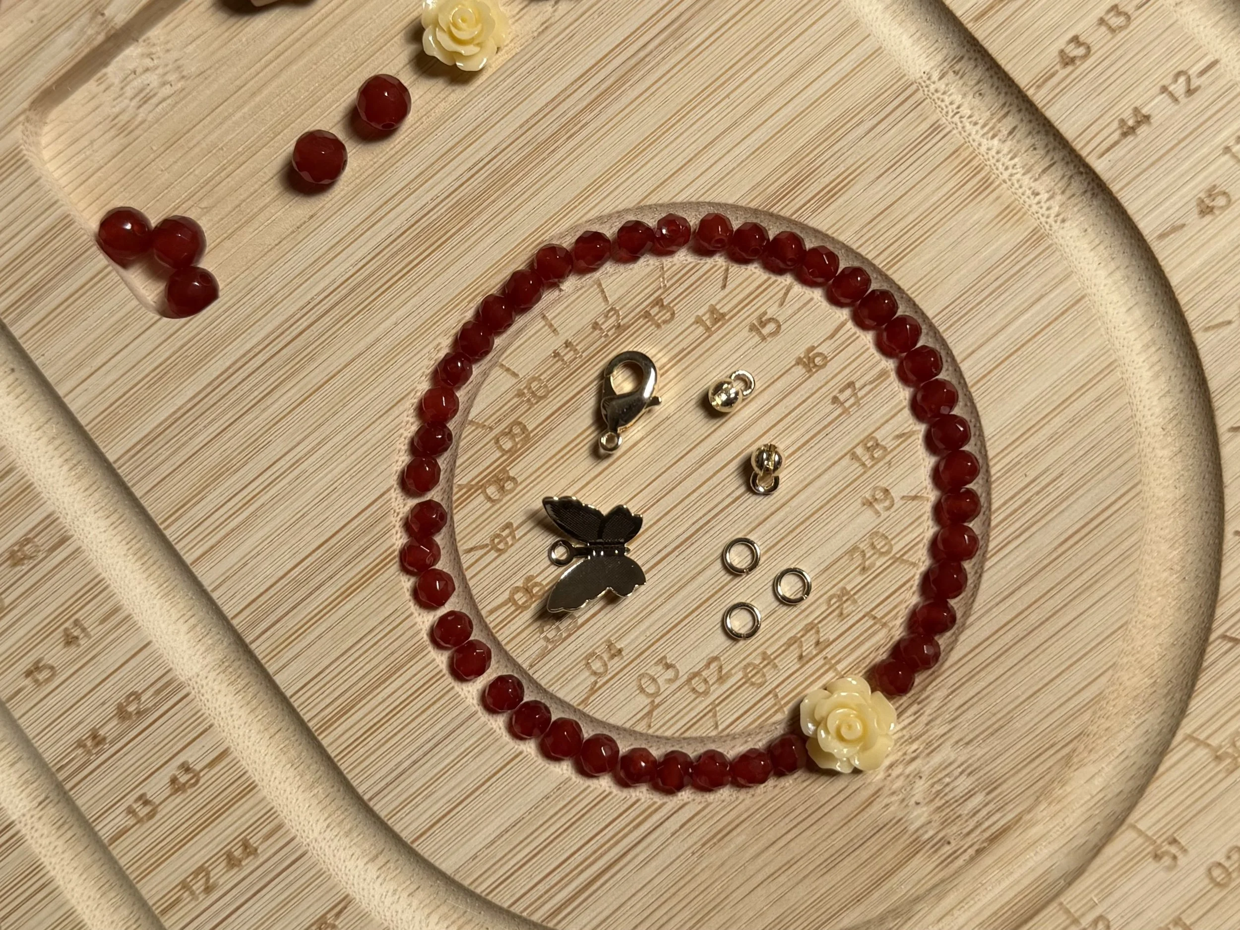 A clock with a heart-shaped outline decorated with red beads and white flowers, positioned on a wooden surface.